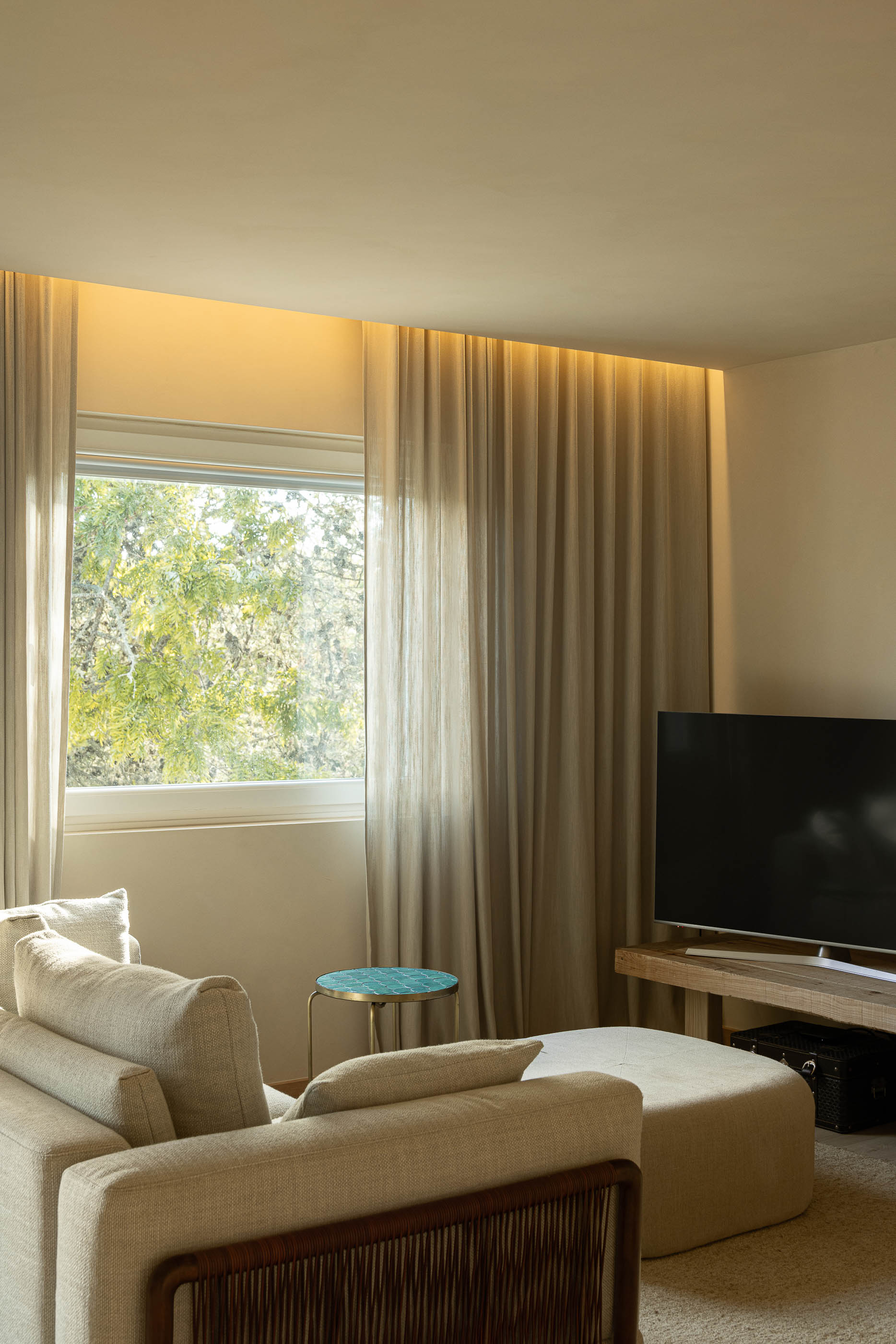 Sala de estar: Sofá em tons neutros, televisão e cortinas claras com iluminação indireta. — Casa de Sintra arquitetura Tsou Arquitectos em Sintra