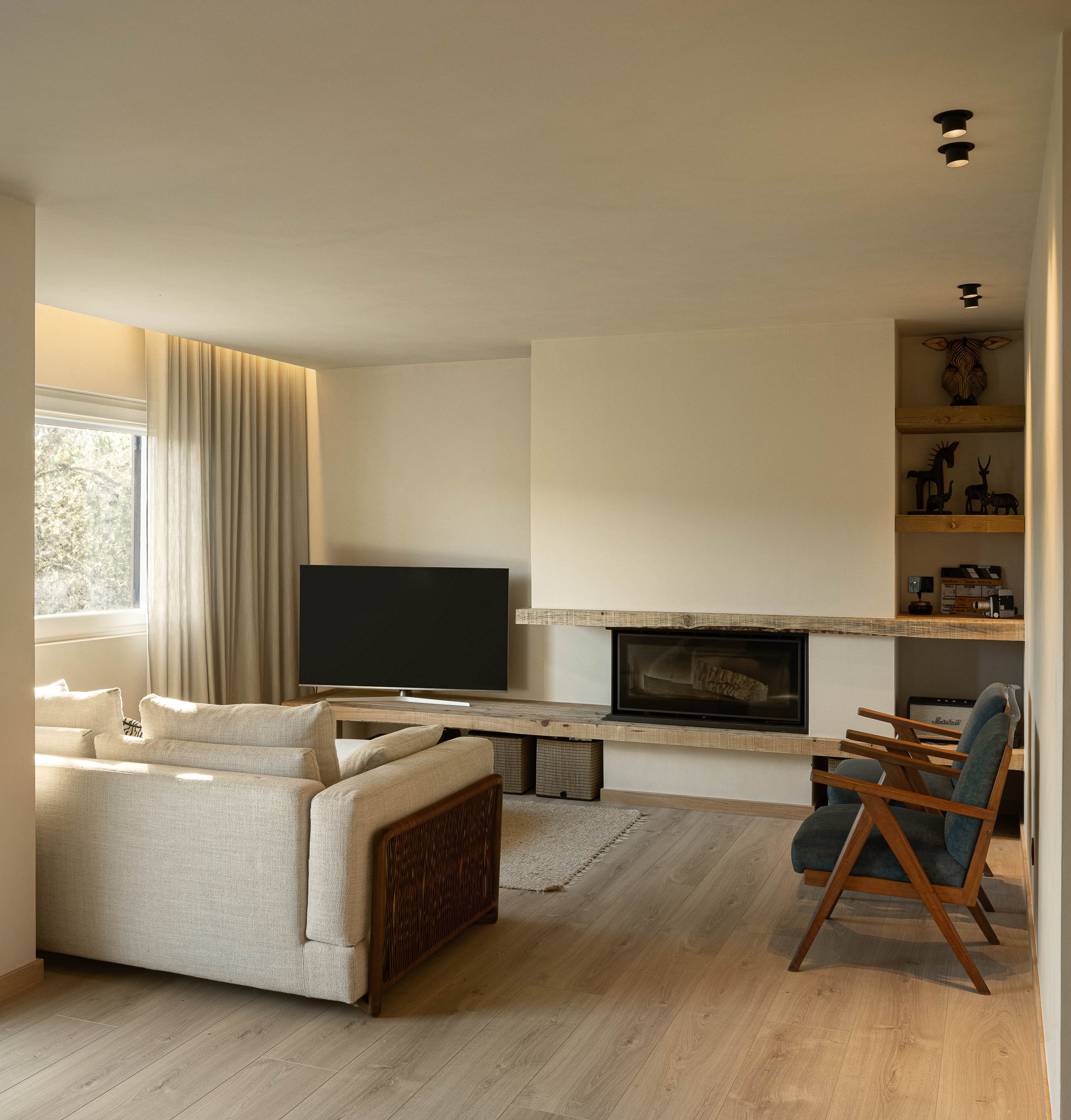 Sala de estar: Lareira embutida, estantes em madeira e cadeirões azuis sobre pavimento em madeira. — Casa de Sintra arquitetura Tsou Arquitectos em Sintra