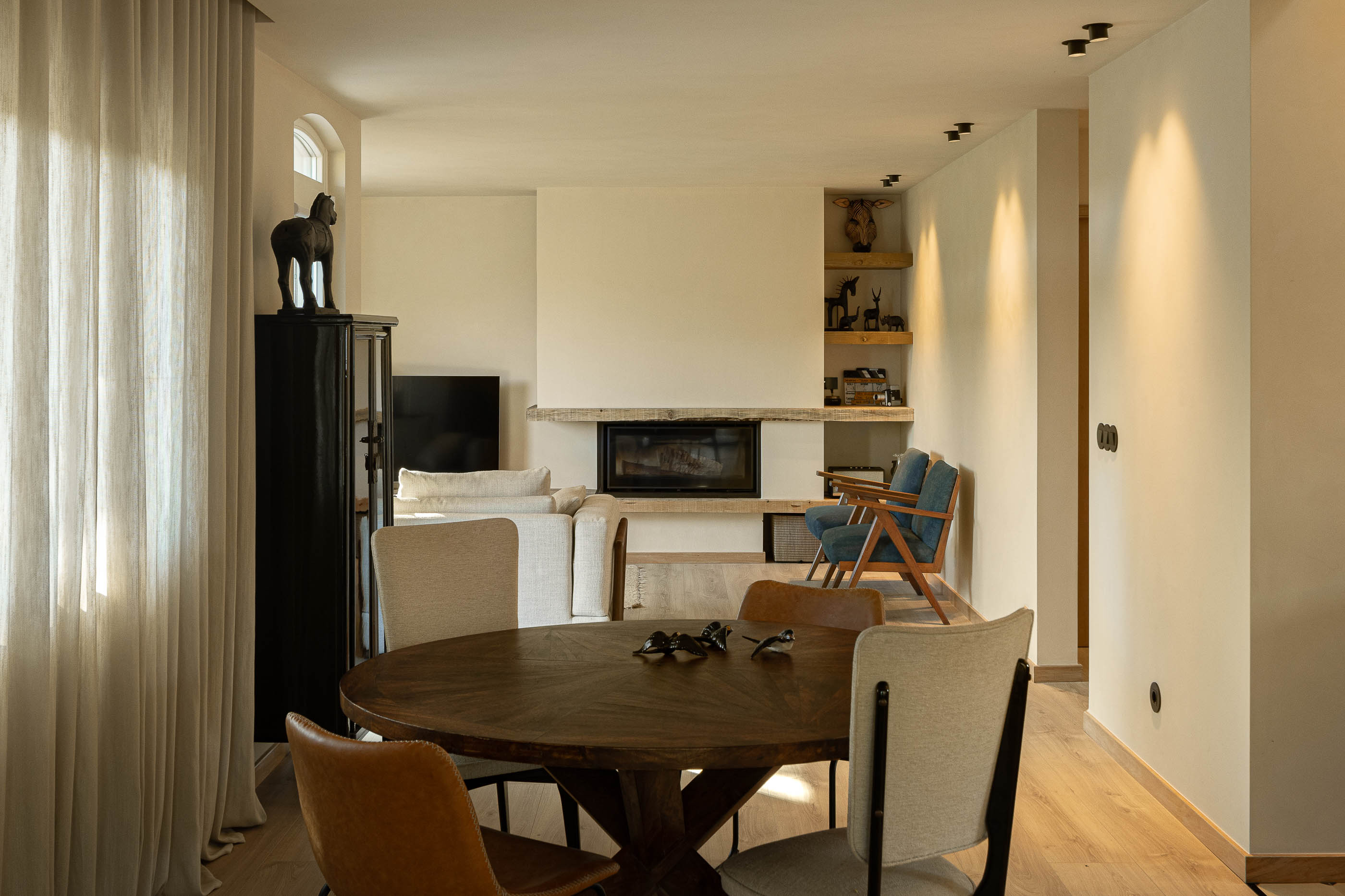 Sala de estar/jantar: Mesa de jantar redonda, lareira e sofá em tons neutros sobre pavimento em madeira. — Casa de Sintra arquitetura Tsou Arquitectos em Sintra