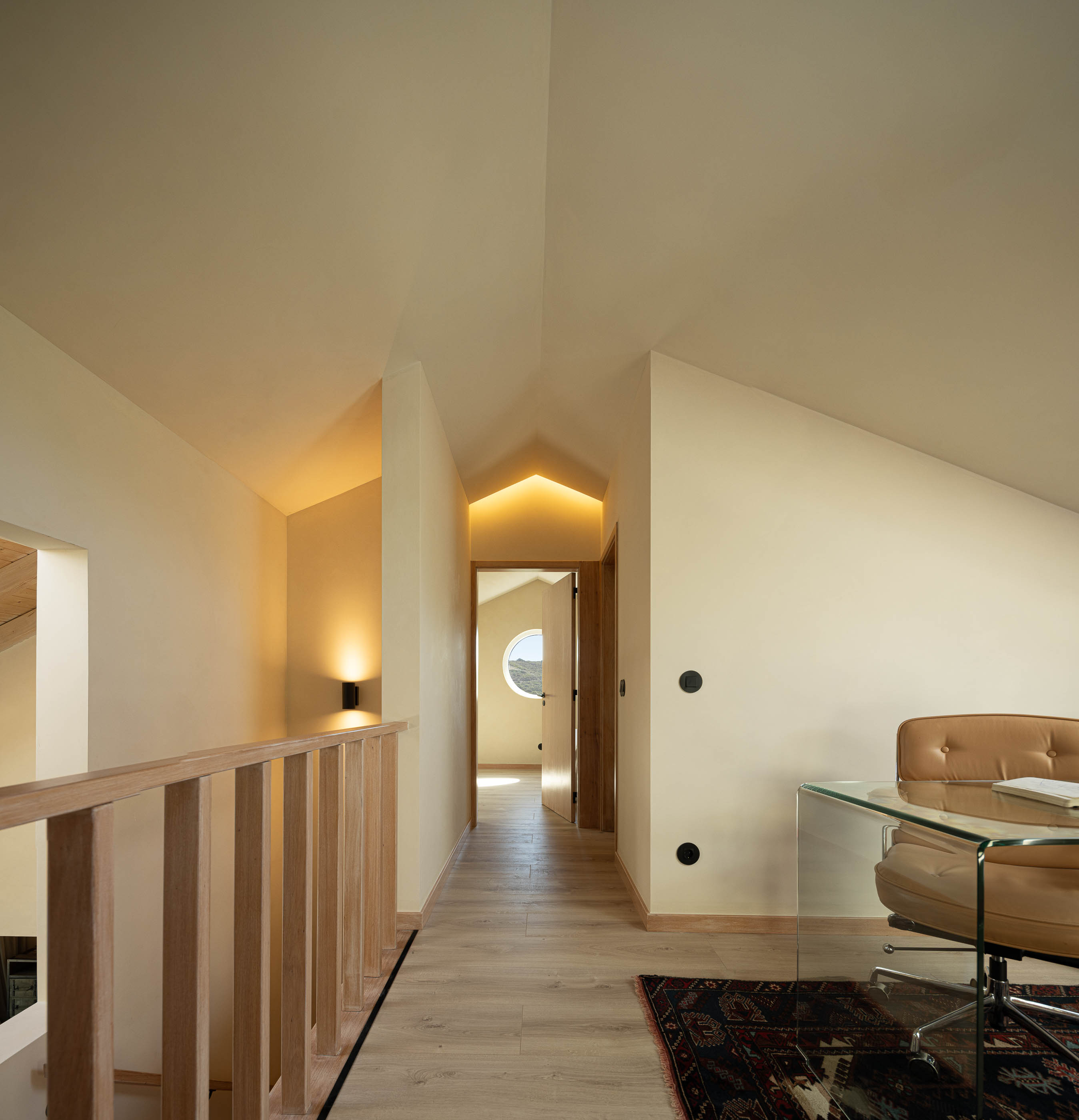 Corredor: Corredor no sótão com pavimento em madeira, secretária e cadeirão em pele. — Casa de Sintra arquitetura Tsou Arquitectos em Sintra
