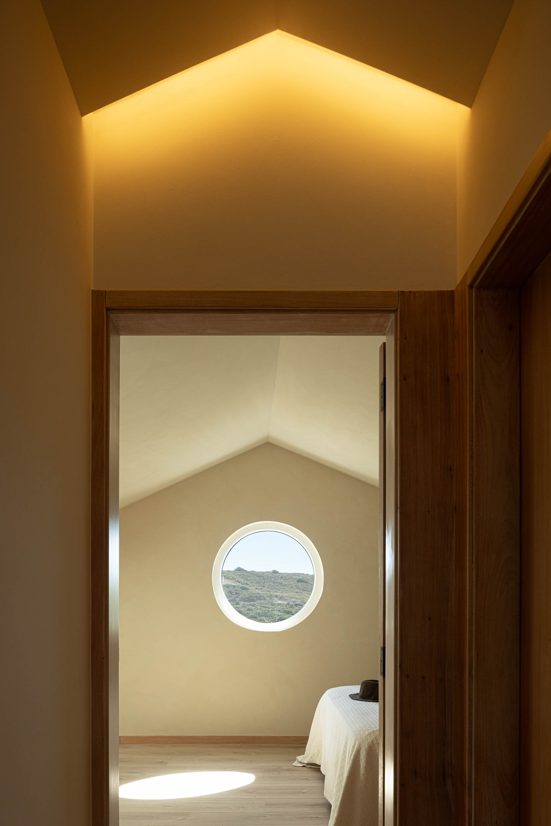 Quarto: Porta com vista para quarto com janela redonda e cama com colcha branca. — Casa de Sintra arquitetura Tsou Arquitectos em Sintra