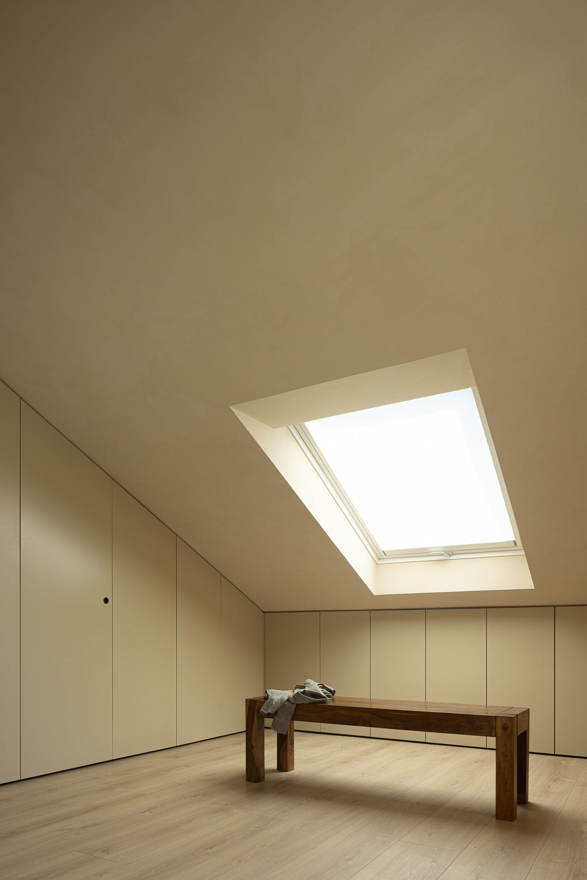 Quarto: Quarto no sótão com janela no teto, banco em madeira e pavimento em madeira clara. — Casa de Sintra arquitetura Tsou Arquitectos em Sintra