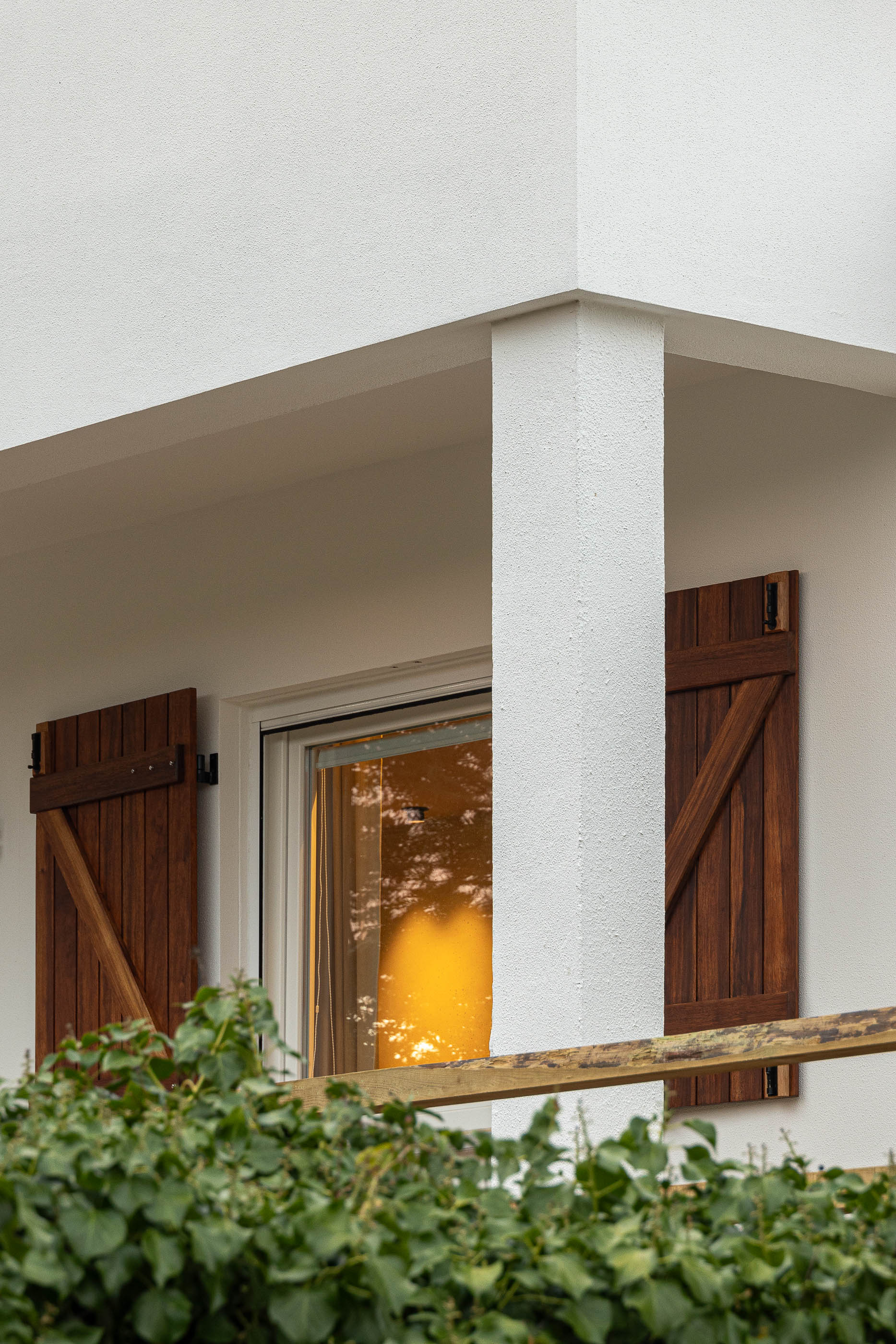 Exterior: Fachada branca com janela protegida por portadas em madeira escura e vegetação. — Casa de Sintra arquitetura Tsou Arquitectos em Sintra