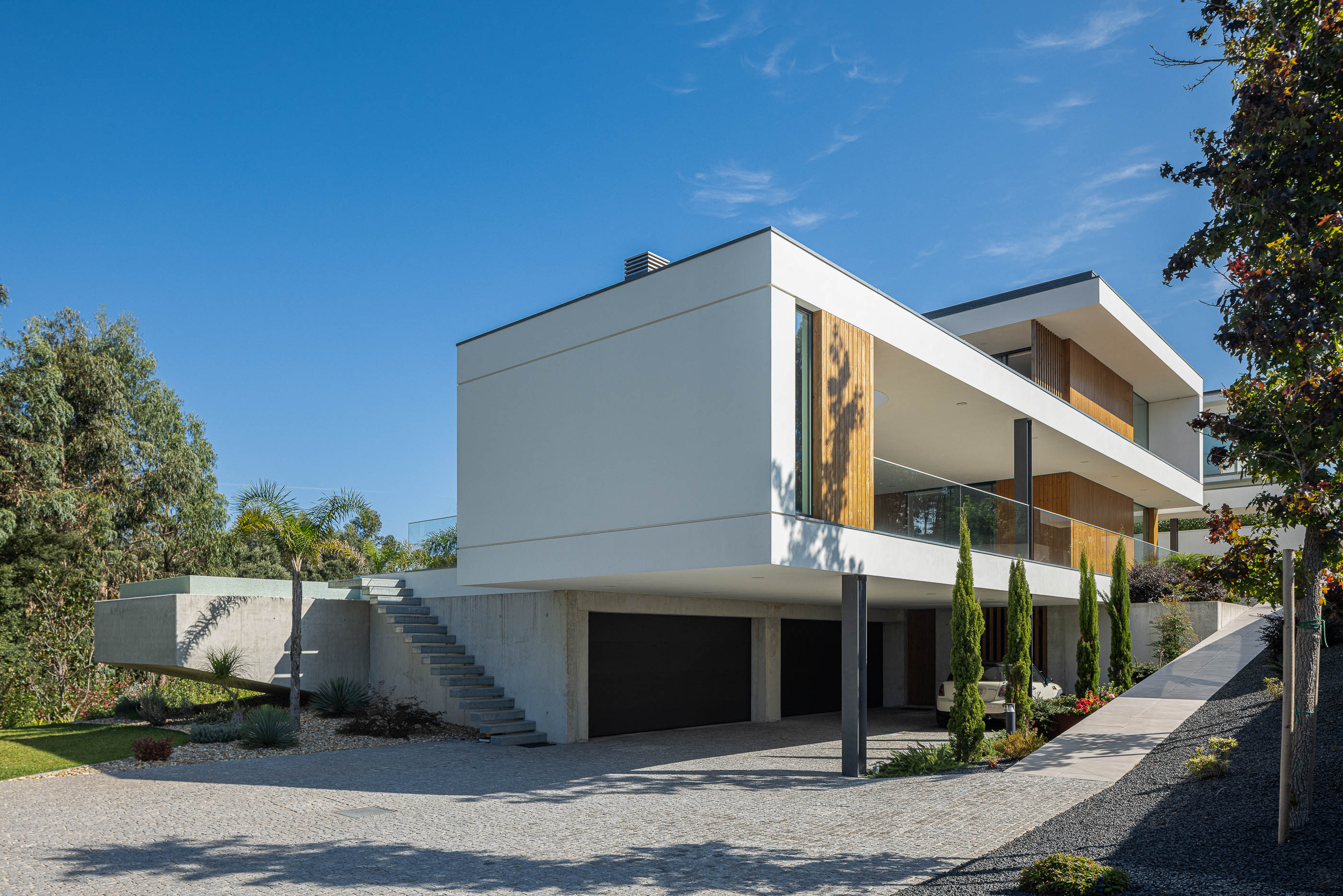 Exterior: Fachada posterior da casa com piscina, garagem e acesso pedonal, arquitetura moderna em betão e madeira. — Casa J.M.C. arquitetura Atelier d´Arquitectura Lopes da Costa em Santa Maria da Feira