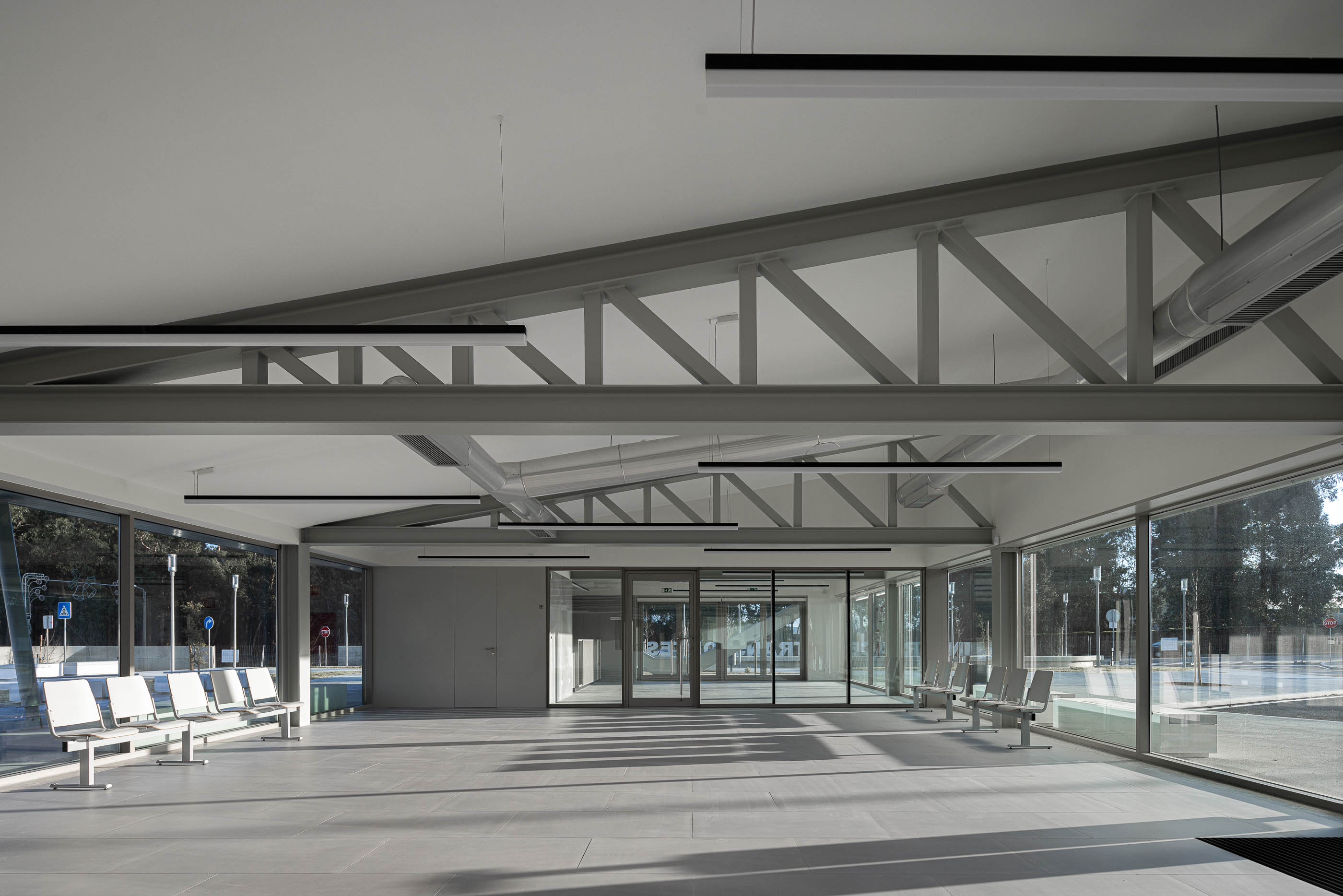 Interior: Sala de espera com estrutura metálica exposta, pavimento cinzento e bancos metálicos. — Interface de Transportes Lourosa-Fiães arquitetura Atelier d´Arquitectura Lopes da Costa em Santa Maria da Feira