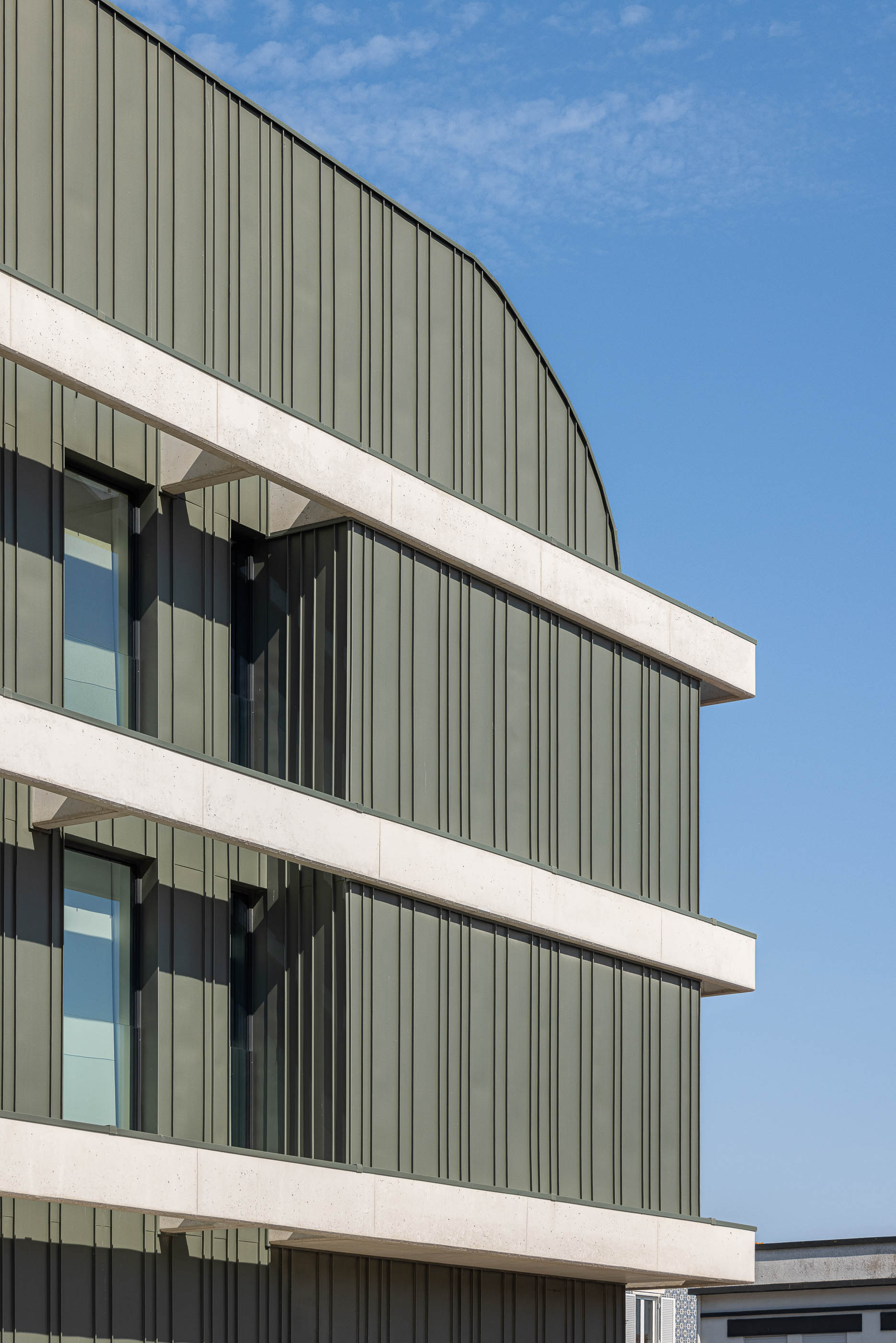 Fachada: Detalhe da fachada com revestimento em painéis verticais cinzentos, elementos horizontais em betão e janelas. — Edifício LUX arquitetura Mário Alves Arquitecto em Ílhavo
