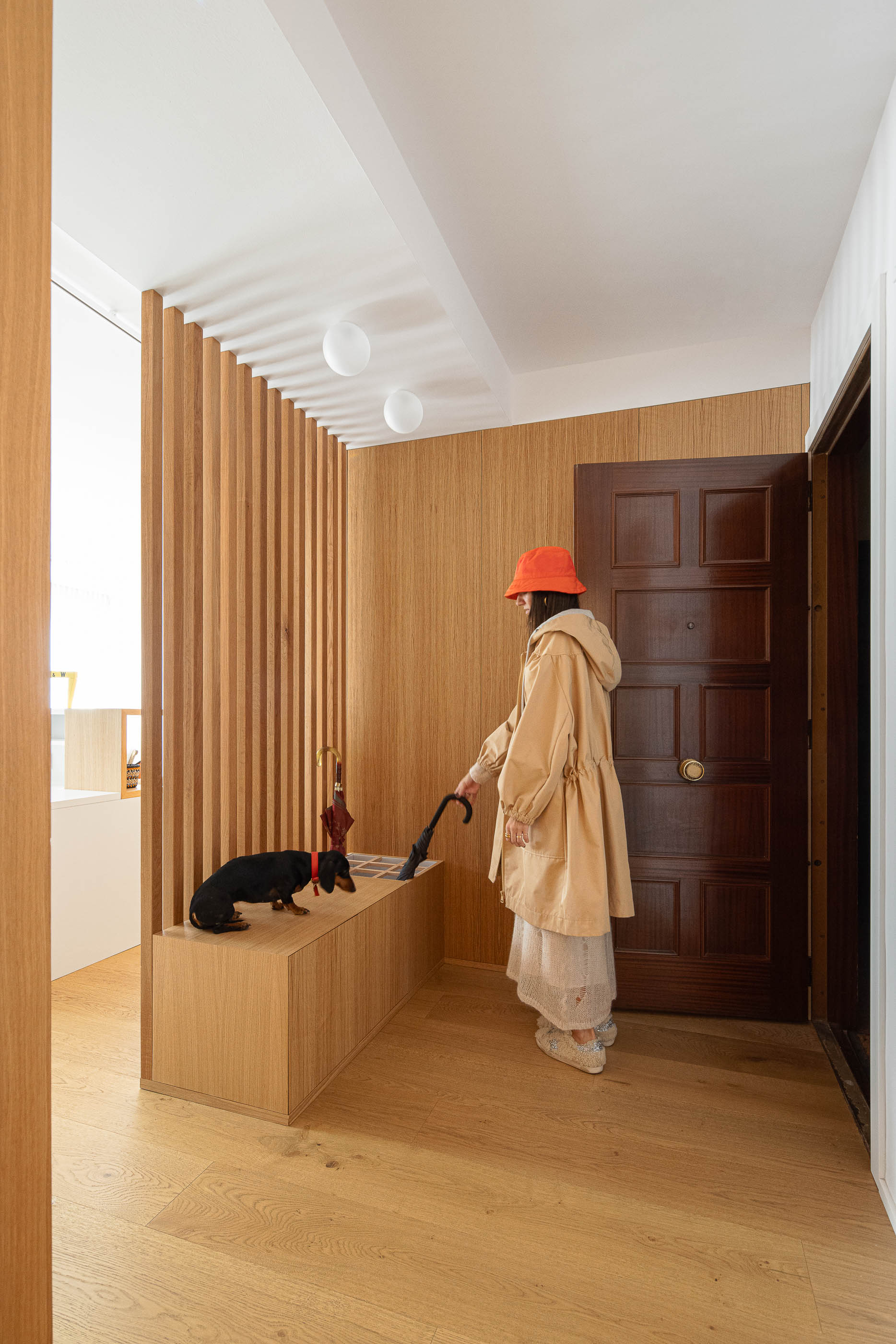 Hall de entrada com porta de madeira escura, biombo de ripas de madeira clara e banco embutido. Pavimento em madeira clara. — Reforma Apartamento CV em Avilés arquitetura David Olmos Arquitectos em Avilés