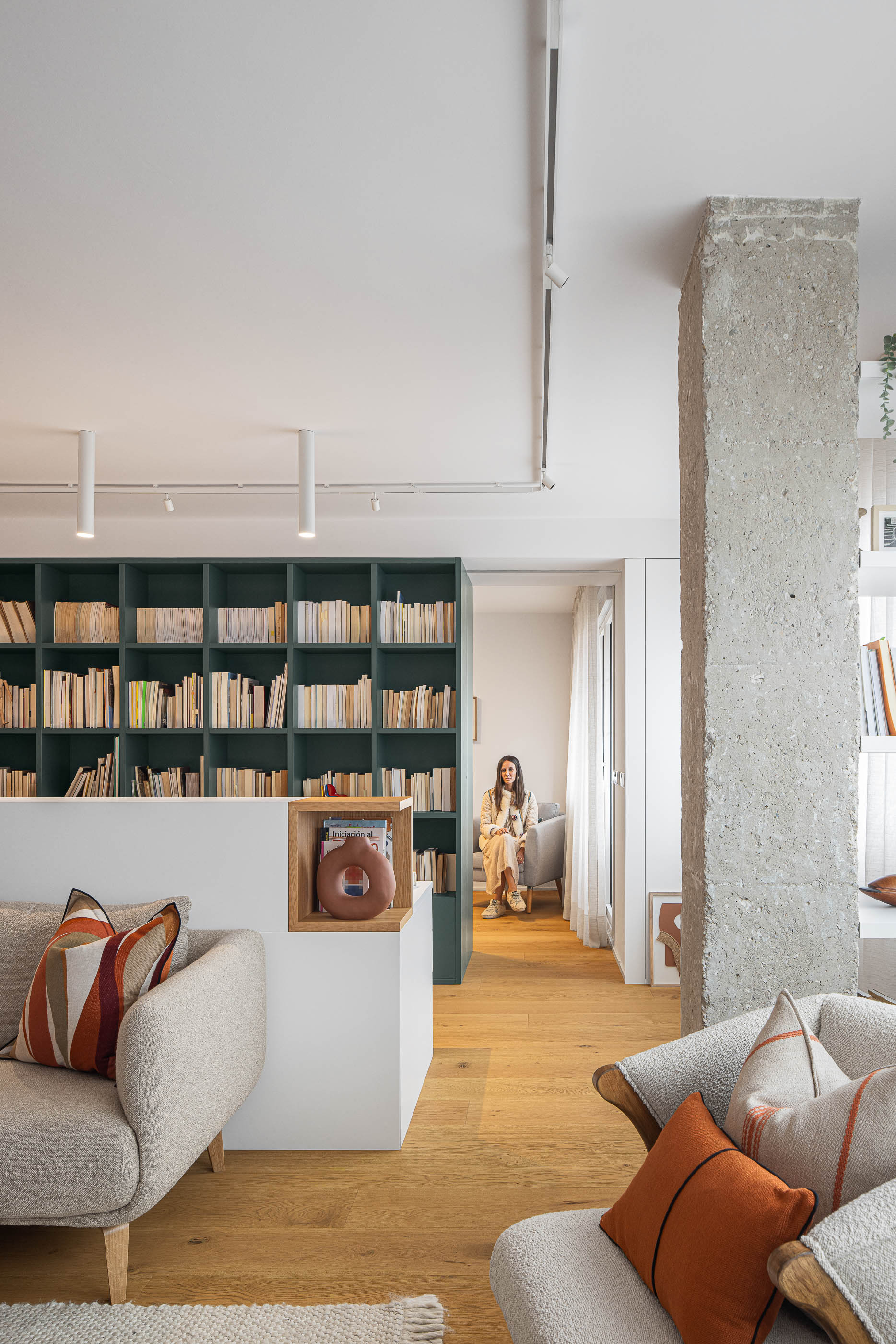 Sala de estar com estante verde escura, pilar de betão aparente e pavimento em madeira clara. Sofás e cadeirões com almofadas coloridas. — Reforma Apartamento CV em Avilés arquitetura David Olmos Arquitectos em Avilés