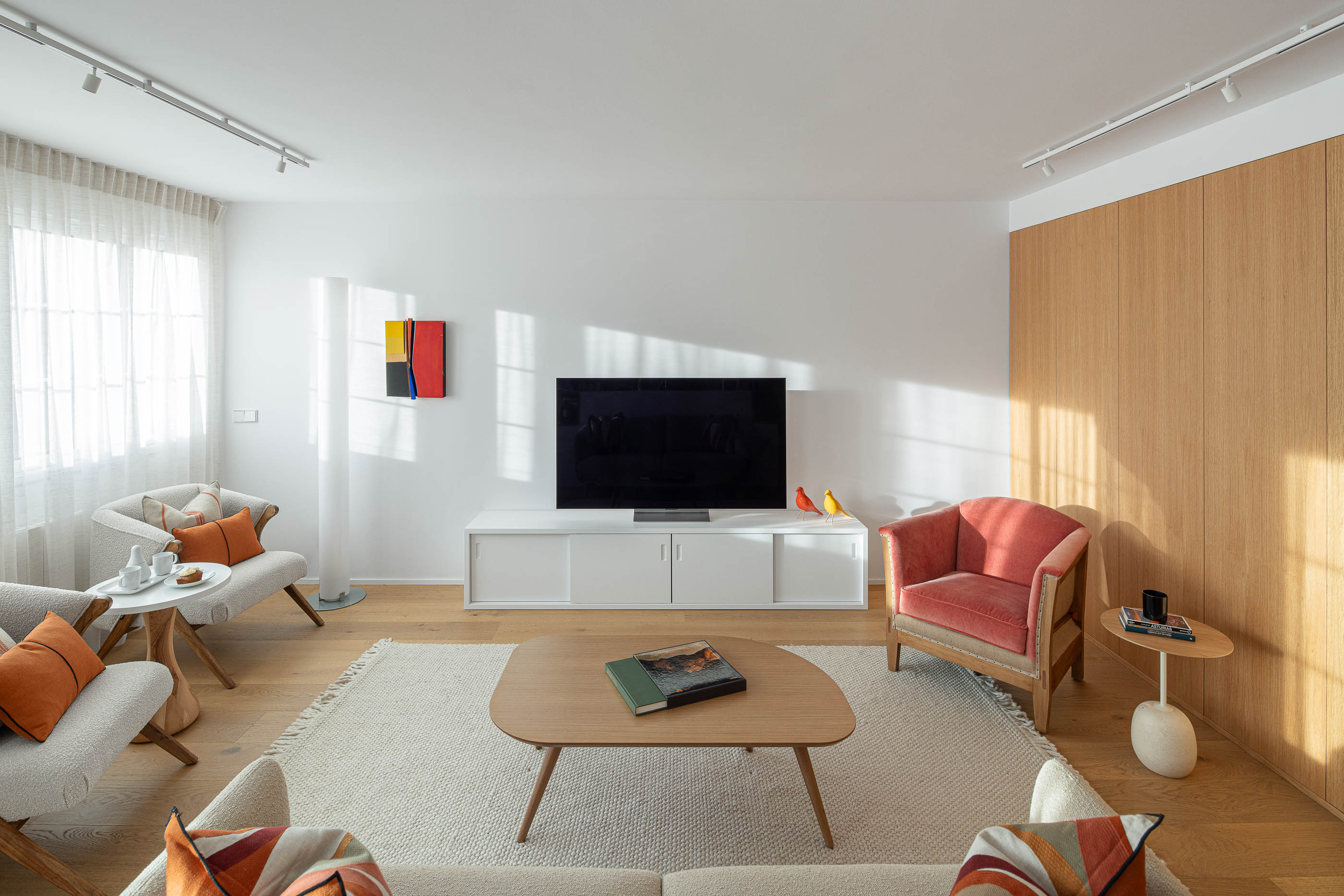 Sala de estar com cadeirões, mesa de centro e móvel de televisão branco. Pavimento em madeira clara e cortinas brancas. — Reforma Apartamento CV em Avilés arquitetura David Olmos Arquitectos em Avilés