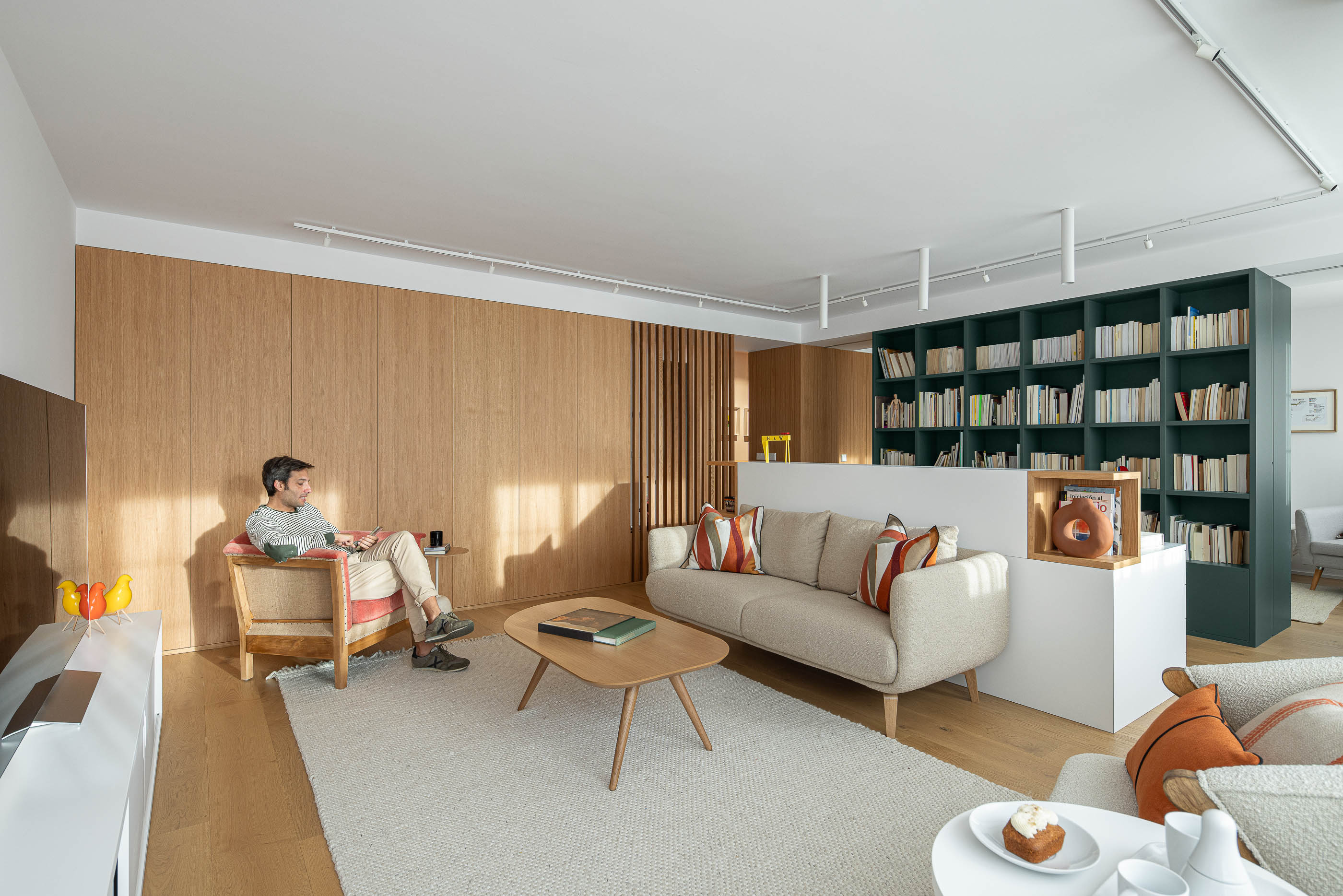 Sala de estar com sofá cinzento, cadeirão de madeira e estante verde escura. Pavimento em madeira clara e alcatifa clara. — Reforma Apartamento CV em Avilés arquitetura David Olmos Arquitectos em Avilés