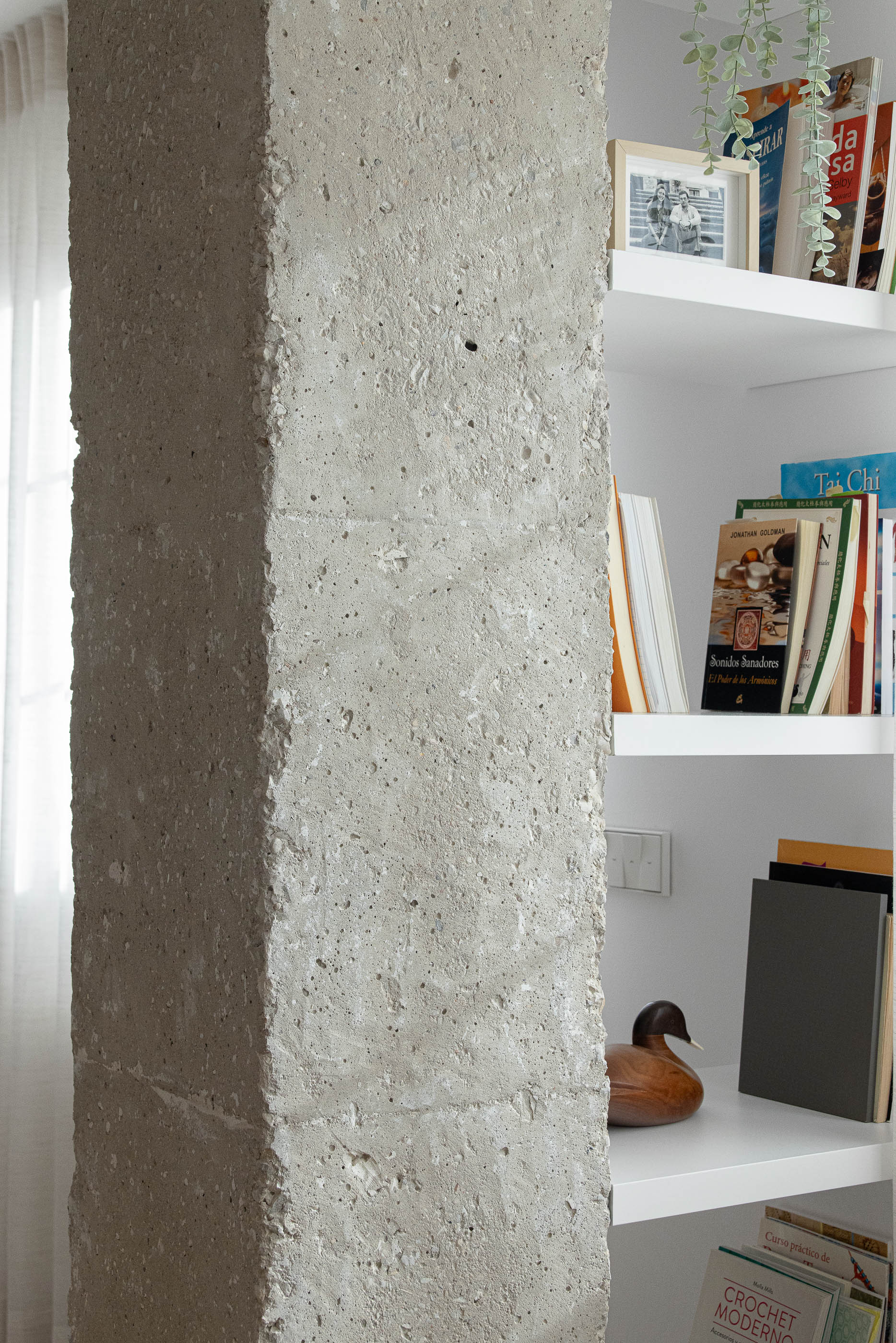 Sala de estar, detalhe do pilar de betão aparente junto a estantes brancas com livros e objetos decorativos. — Reforma Apartamento CV em Avilés arquitetura David Olmos Arquitectos em Avilés