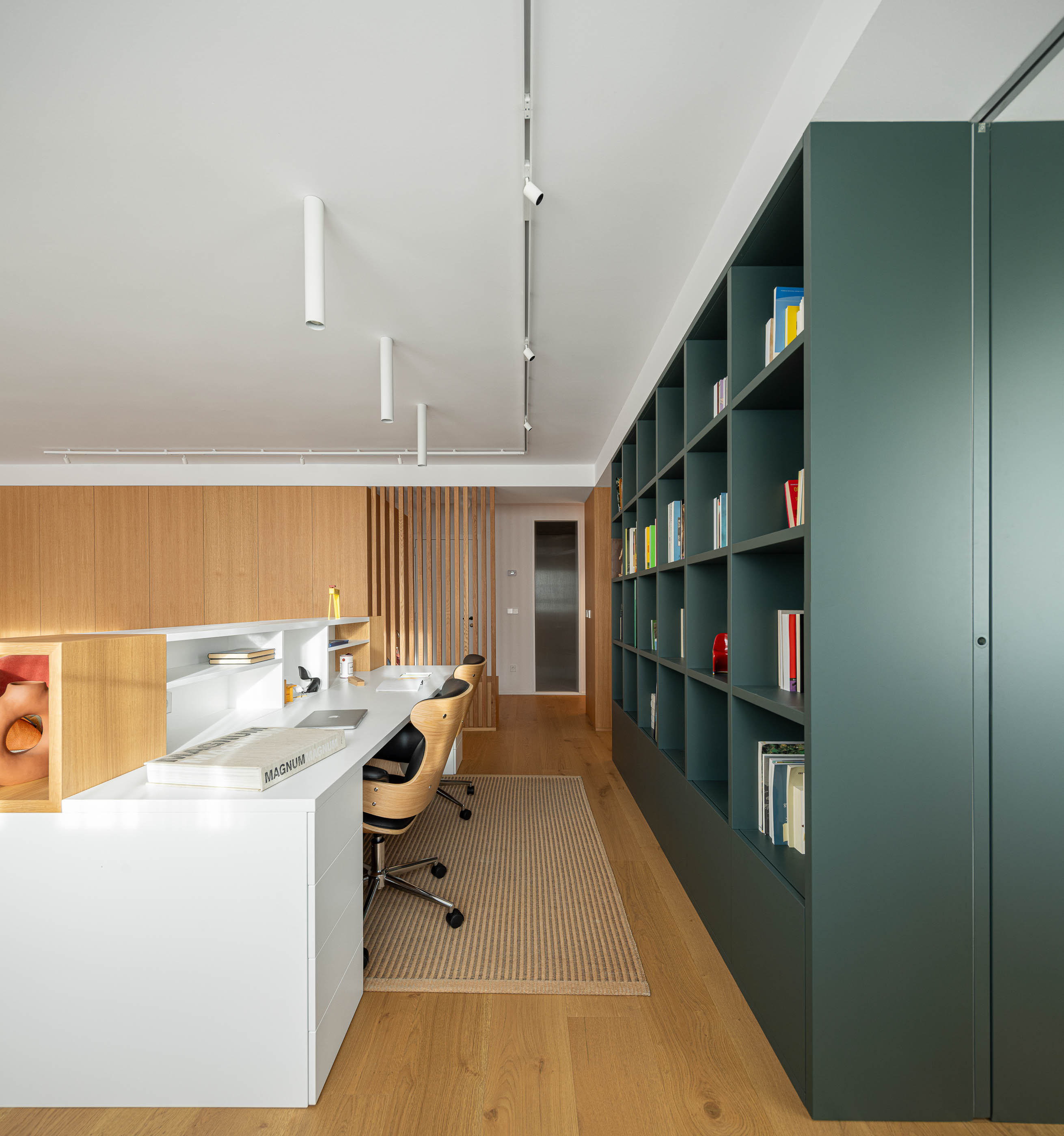 Escritório com secretária branca, cadeiras de madeira e estante verde escura. Pavimento em madeira clara e alcatifa. — Reforma Apartamento CV em Avilés arquitetura David Olmos Arquitectos em Avilés