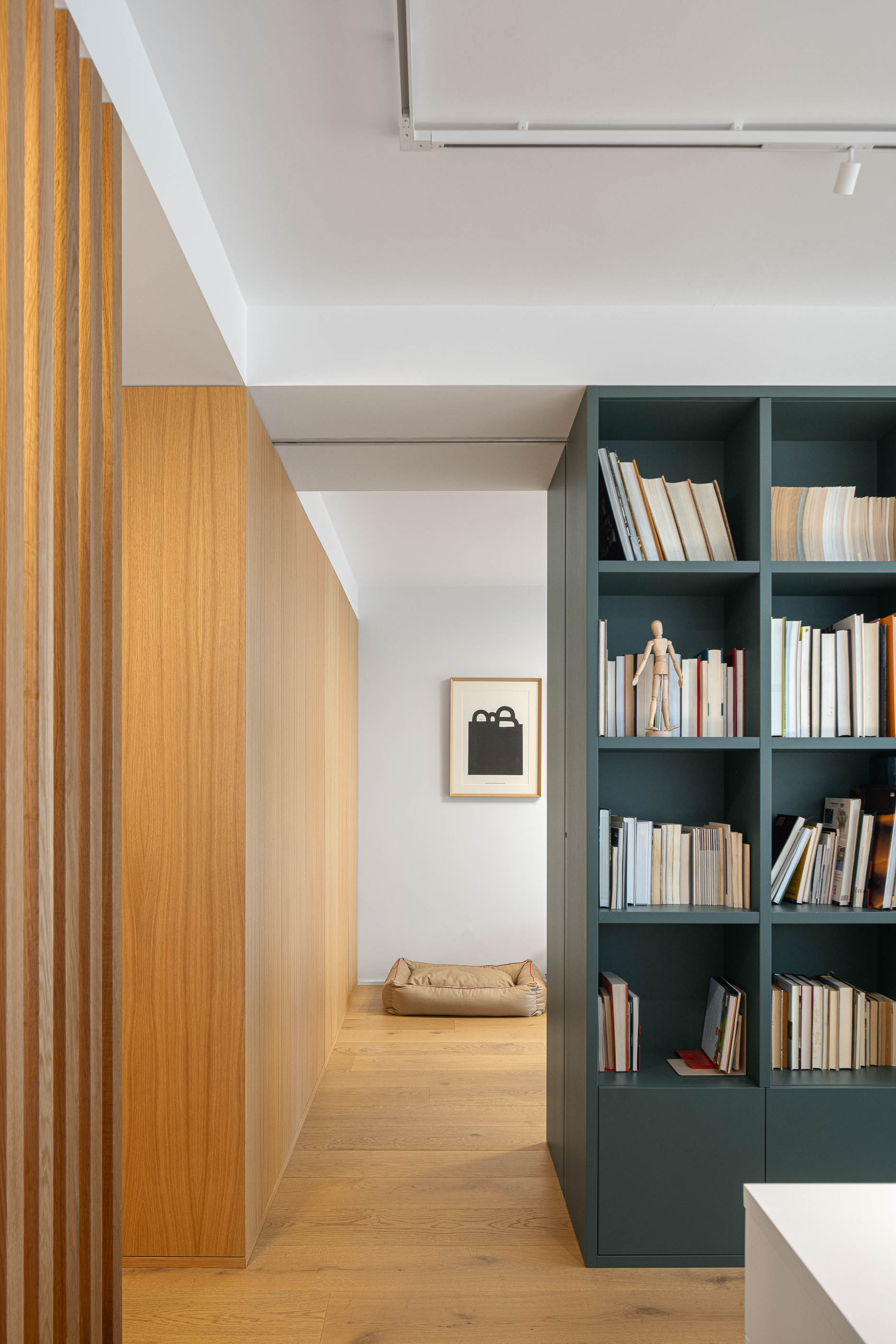 Escritório com estante verde escura e biombo de ripas de madeira clara. Pavimento em madeira clara e parede branca com quadro. — Reforma Apartamento CV em Avilés arquitetura David Olmos Arquitectos em Avilés