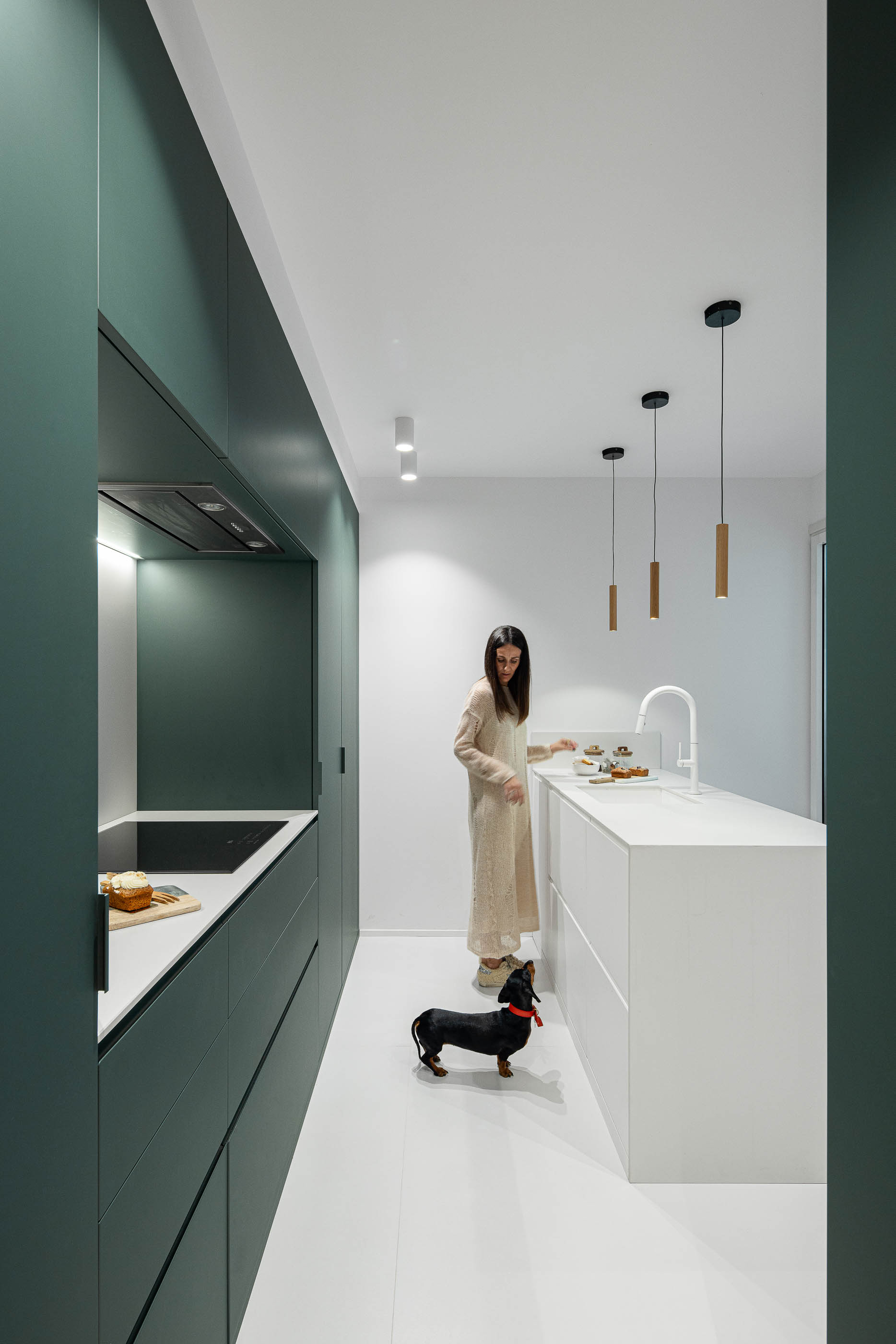 Cozinha com armários verdes escuros, bancada branca e ilha central branca. Pavimento branco e candeeiros suspensos. — Reforma Apartamento CV em Avilés arquitetura David Olmos Arquitectos em Avilés