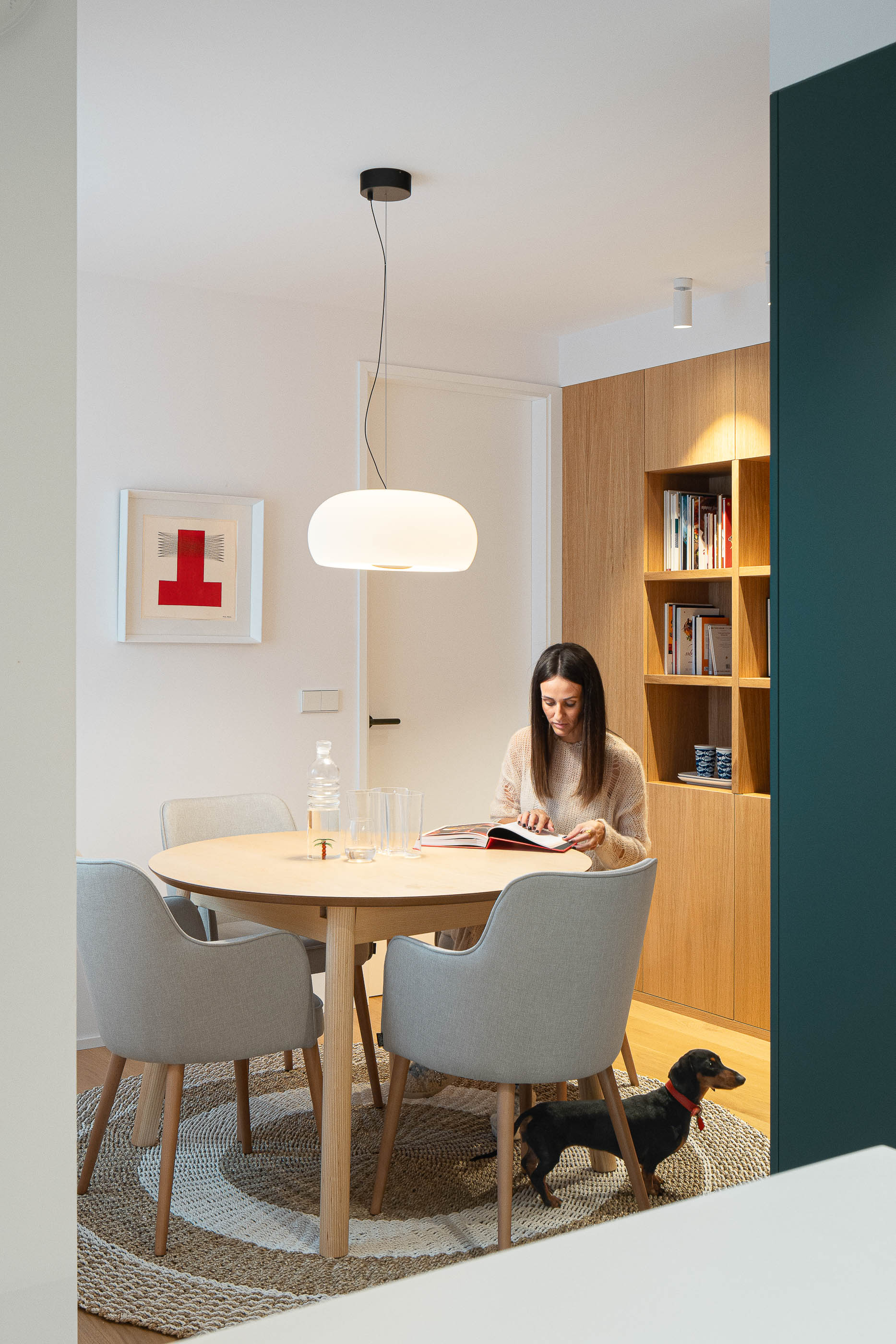 Sala de jantar com mesa redonda de madeira, cadeiras cinzentas e candeeiro suspenso branco. Pavimento em madeira clara e alcatifa. — Reforma Apartamento CV em Avilés arquitetura David Olmos Arquitectos em Avilés