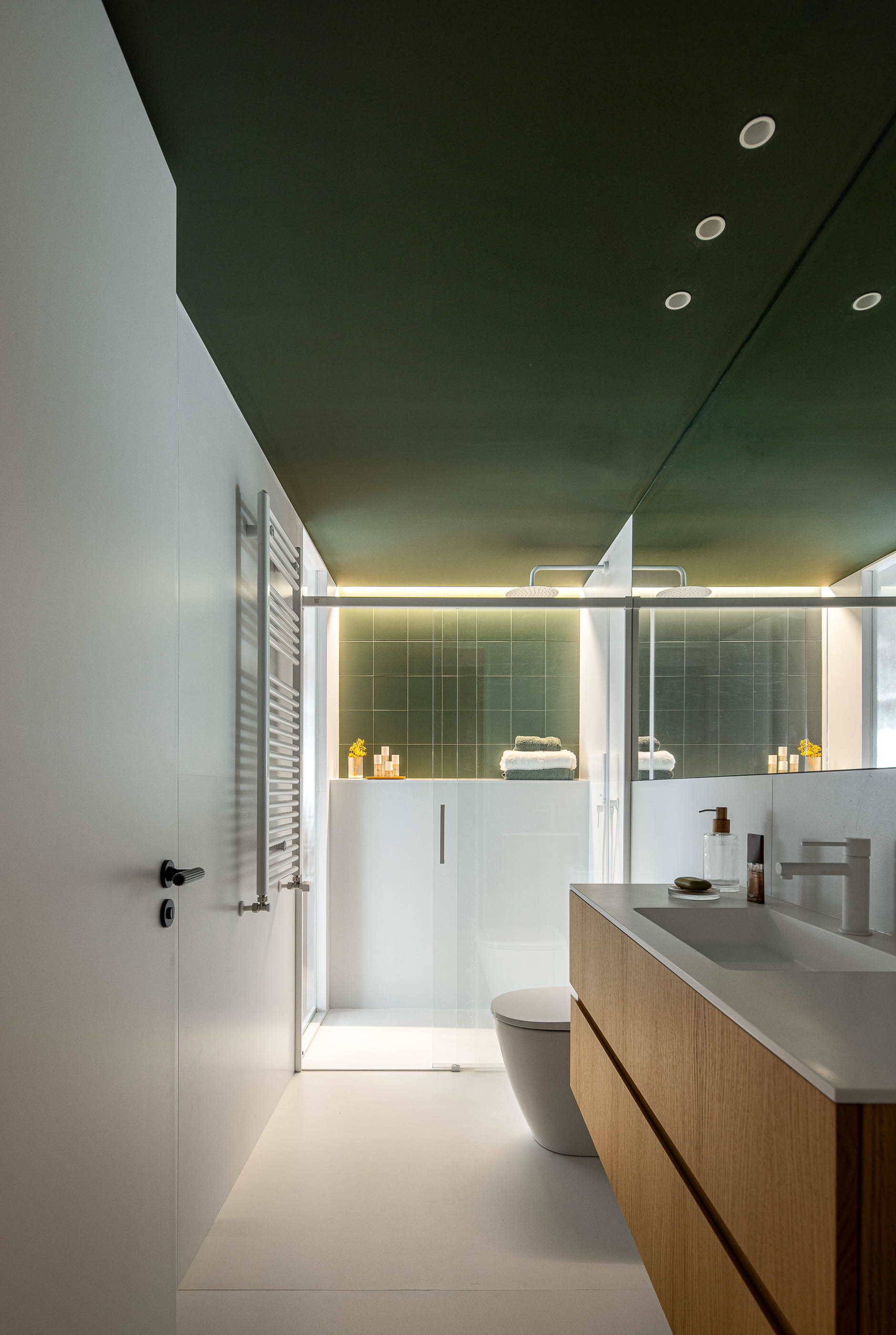 Casa de banho com duche, lavatório com móvel de madeira clara e espelho. Pavimento branco e teto verde escuro. — Reforma Apartamento CV em Avilés arquitetura David Olmos Arquitectos em Avilés