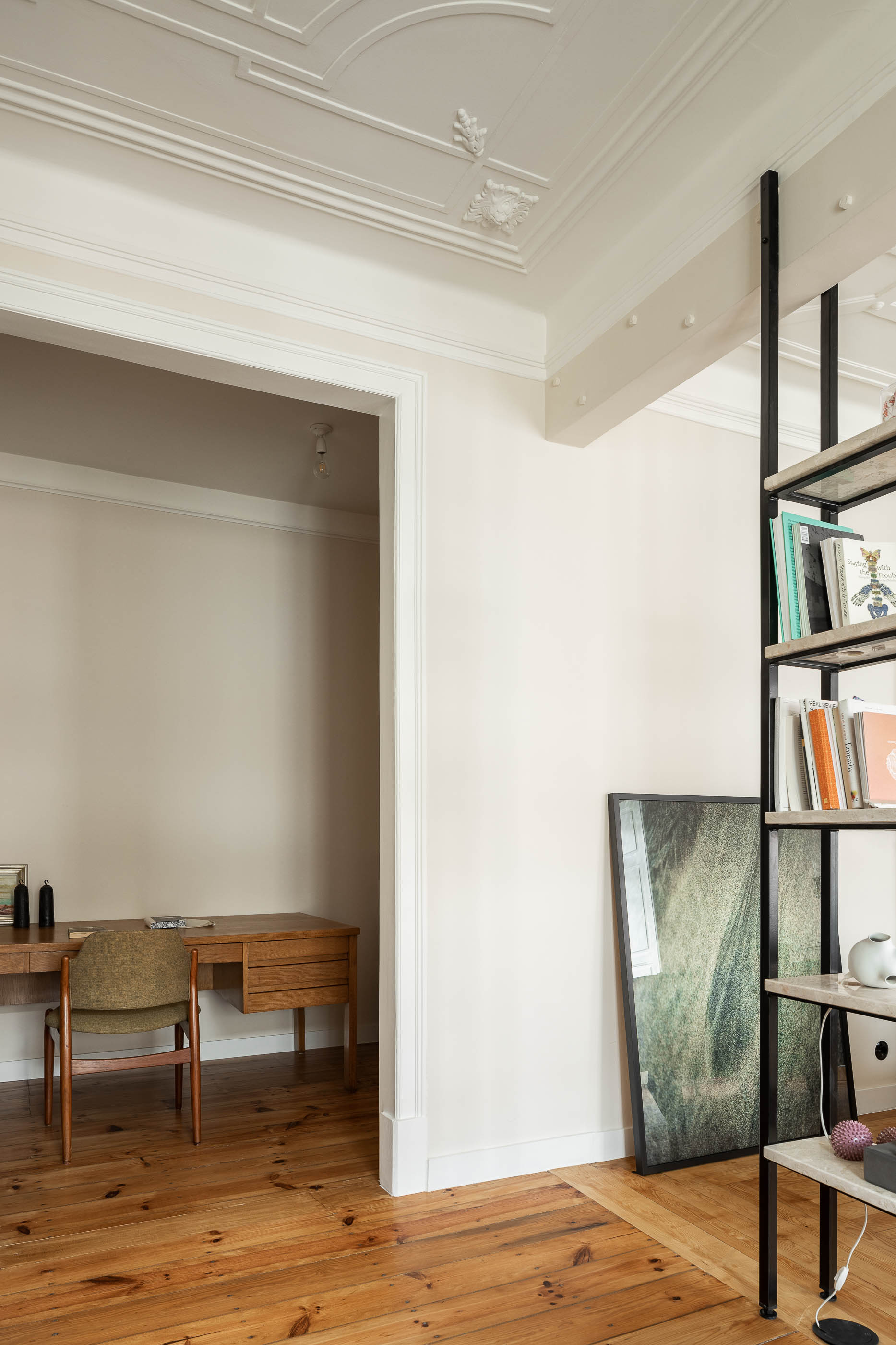 Sala: Secretária de madeira clássica e cadeira verde, pavimento em madeira, estante metálica com prateleiras em pedra. — Apartamento da Penha arquitetura Paulo Moreira Architectures em Lisboa