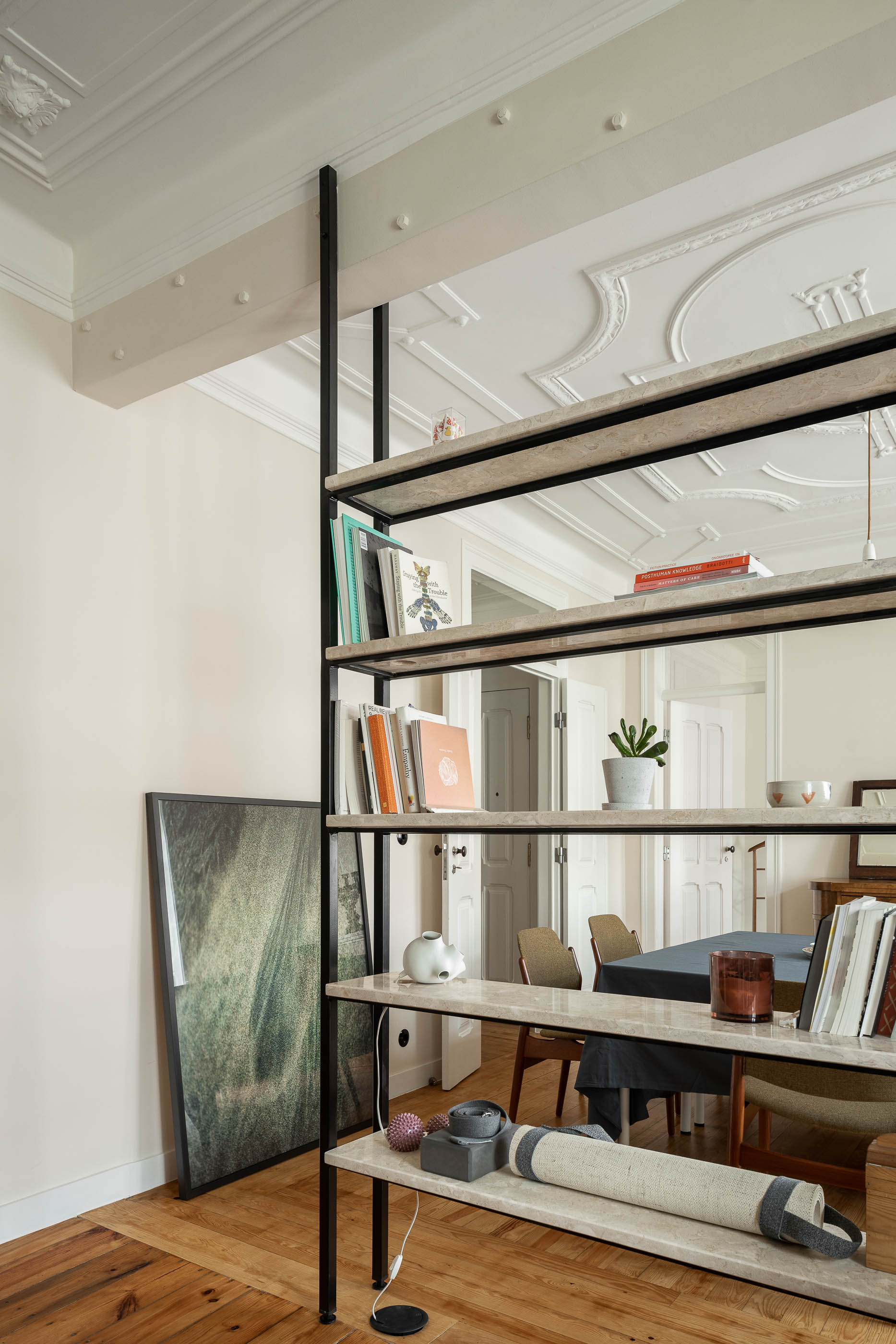 Sala: Estante metálica com prateleiras em pedra, pavimento em madeira, tecto trabalhado, mesa de jantar ao fundo. — Apartamento da Penha arquitetura Paulo Moreira Architectures em Lisboa