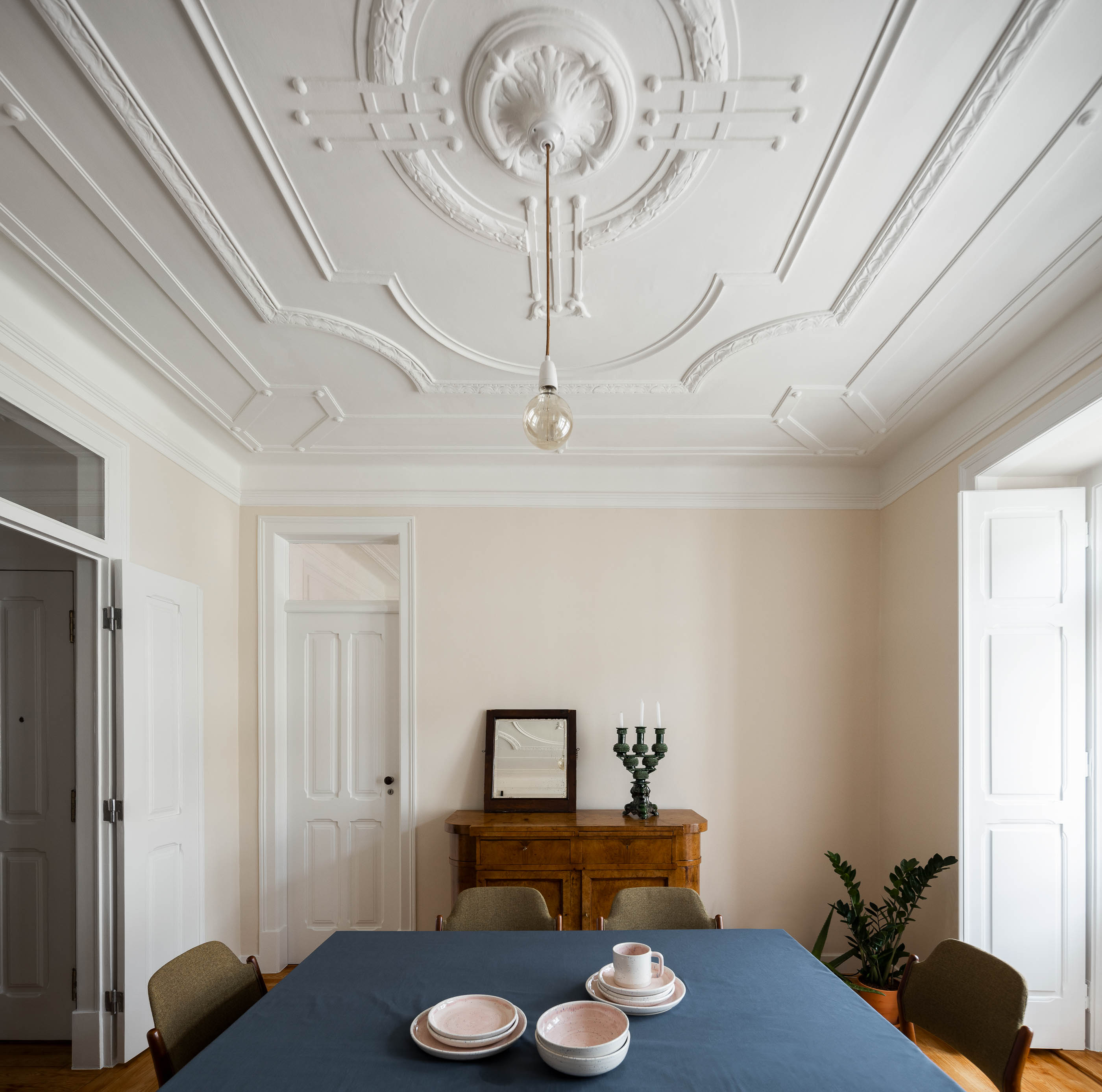 Sala de jantar: Tecto trabalhado com candeeiro pendurado, mesa de madeira com toalha azul, aparador antigo. — Apartamento da Penha arquitetura Paulo Moreira Architectures em Lisboa