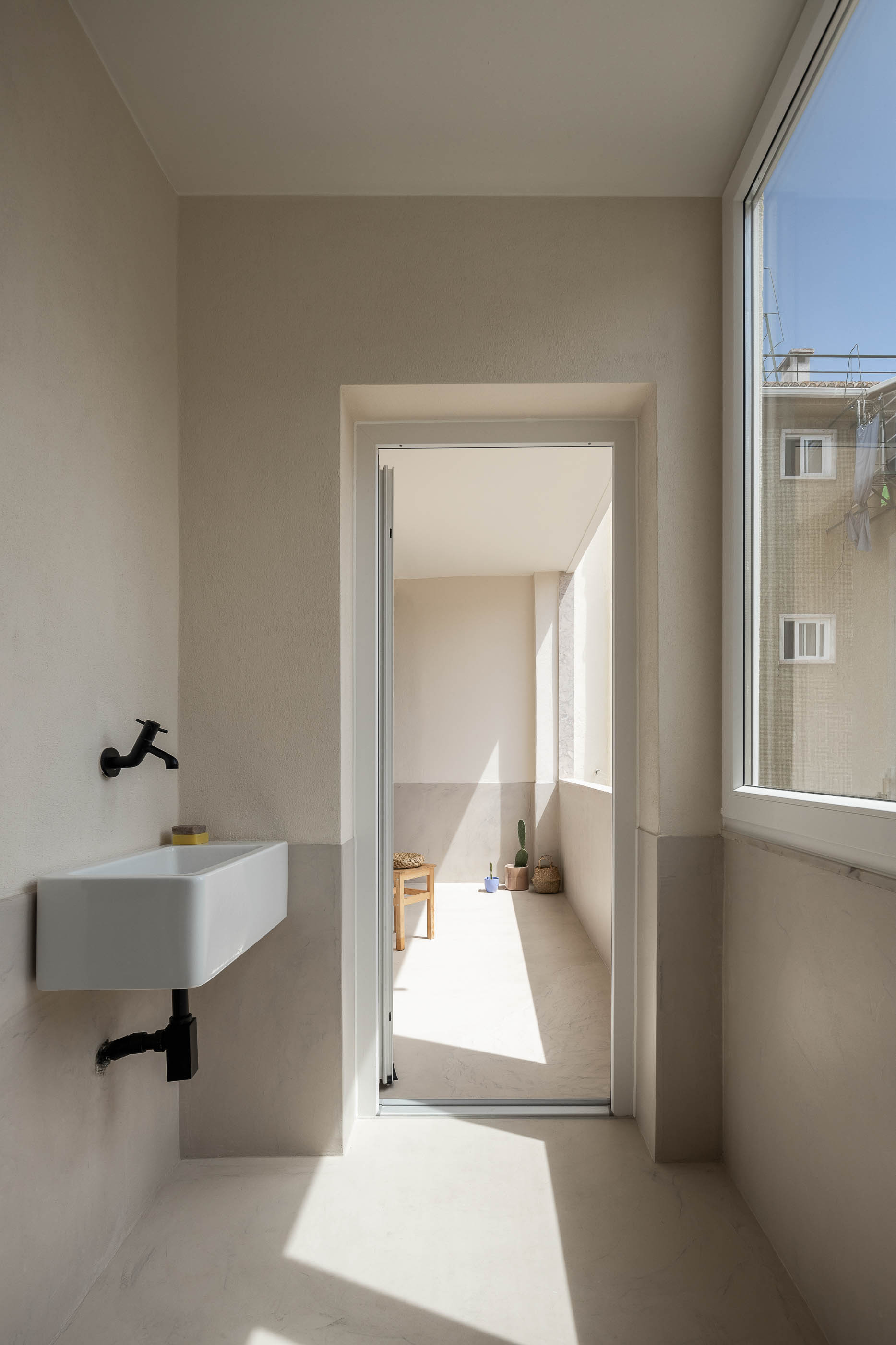 Varanda: Lavatório branco com torneira preta, pavimento claro, porta para o exterior. — Apartamento da Penha arquitetura Paulo Moreira Architectures em Lisboa