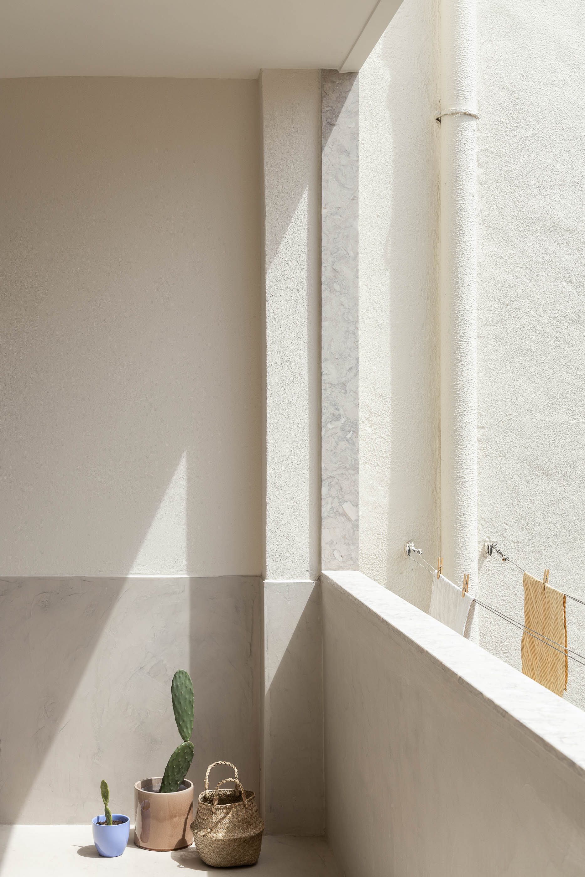 Varanda: Paredes claras, pavimento claro, plantas em vasos, estendal com roupa. — Apartamento da Penha arquitetura Paulo Moreira Architectures em Lisboa