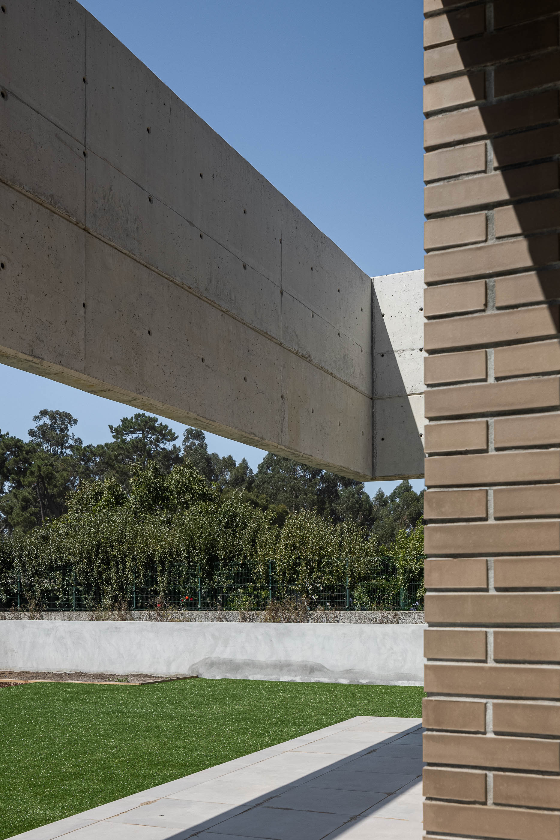 Exterior: Vista do jardim com relvado, caminho em pedra e estrutura em betão e tijolo da casa. — Casa HC arquitetura Sónia Cruz Arquitectura em Aveiro