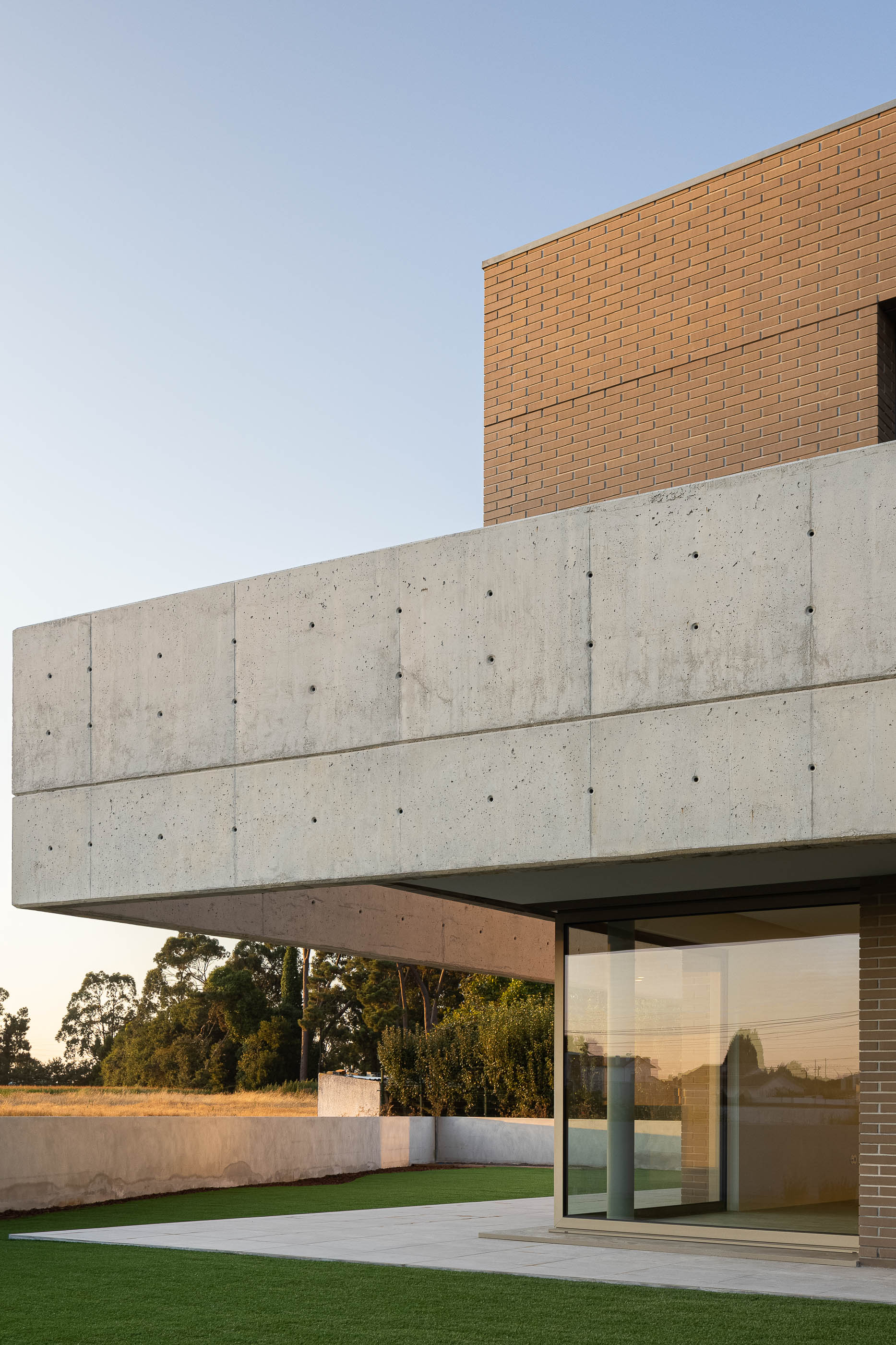 Varanda: Vista da varanda em tijolo com abertura para a paisagem verde ao entardecer. — Casa HC arquitetura Sónia Cruz Arquitectura em Aveiro
