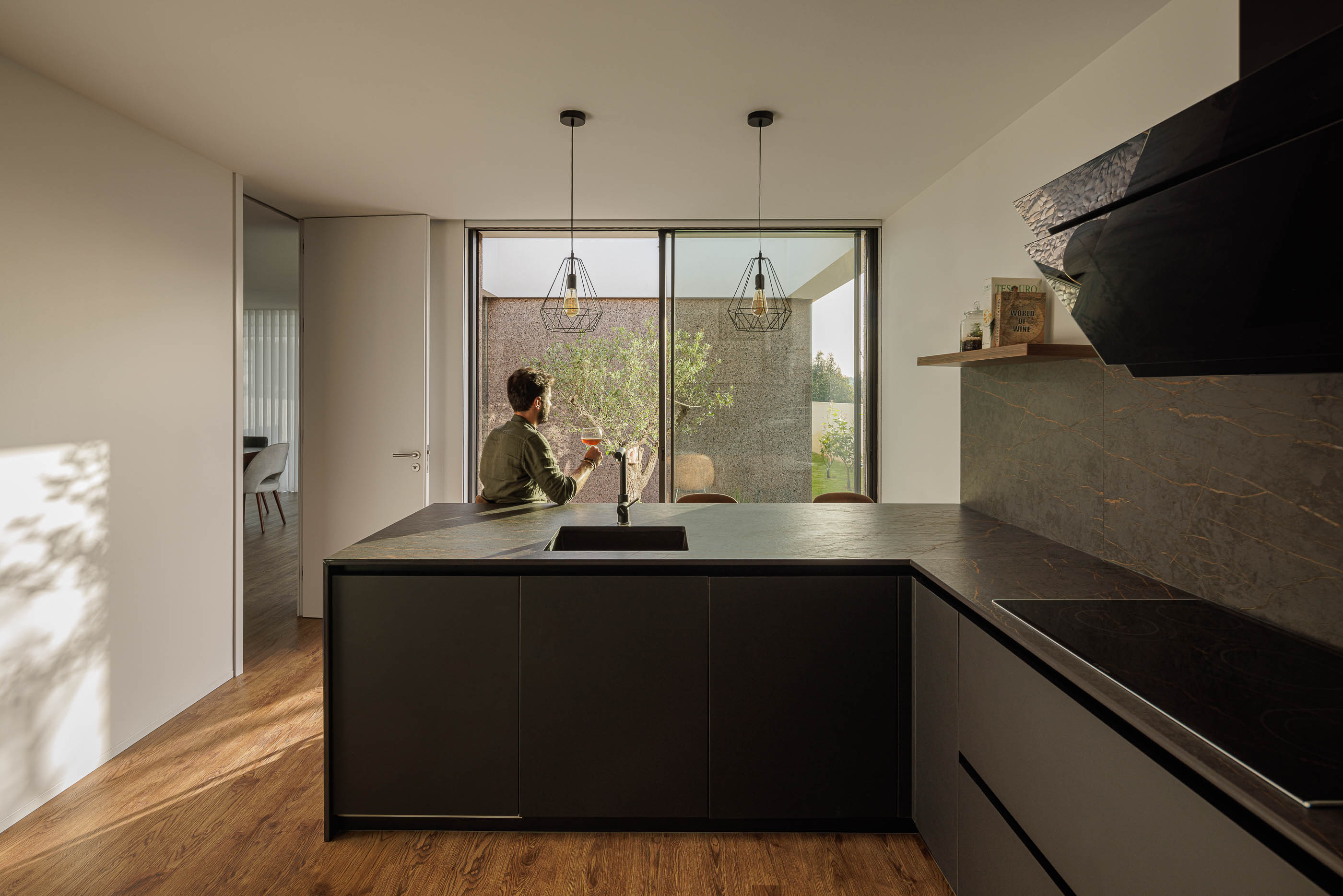 Cozinha: Ilha central com lava-loiça, candeeiros suspensos e vista para o pátio interior. — Casa AS arquitetura Mário Alves Arquitecto em Santa Maria da Feira