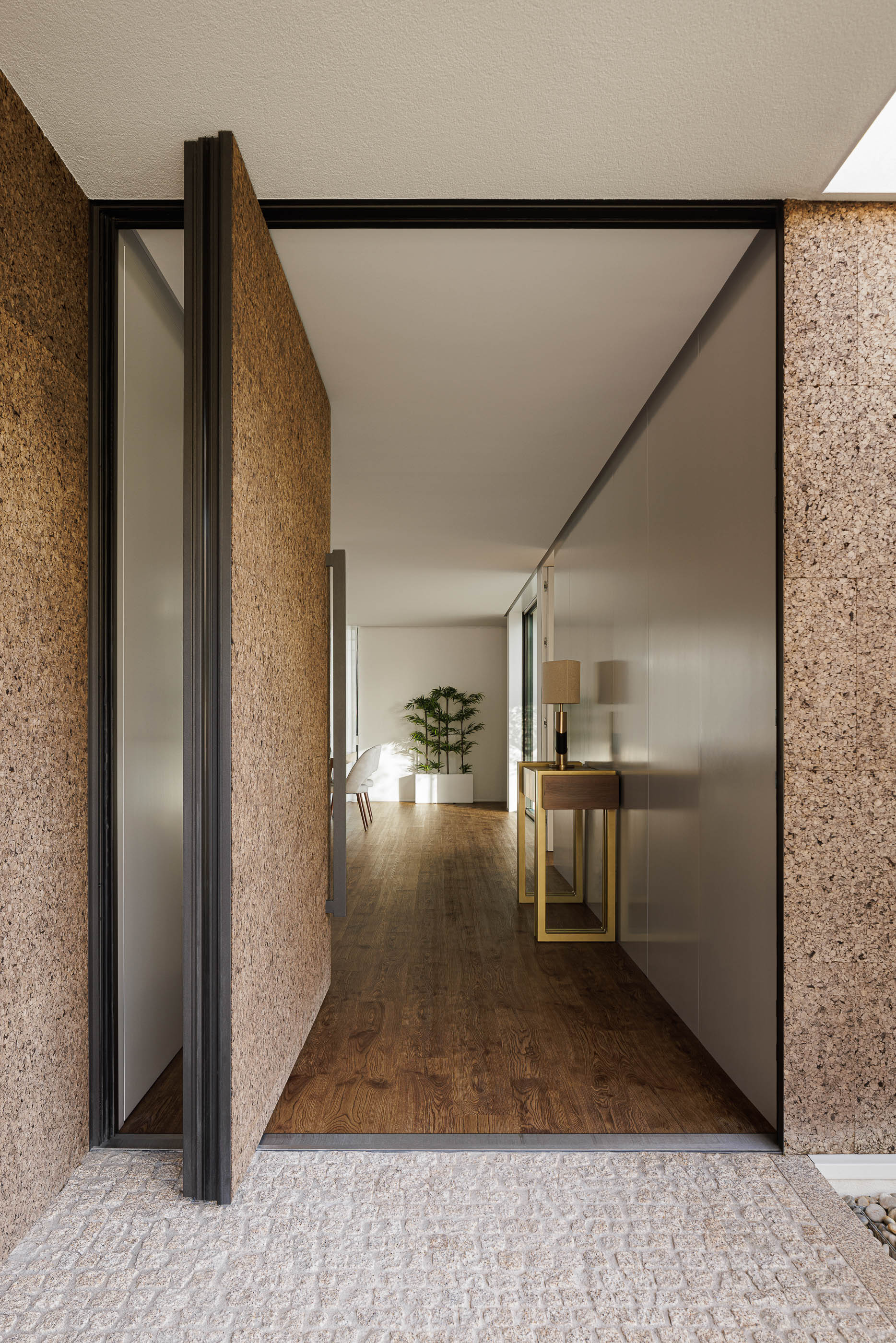 Entrada: Porta pivotante em cortiça, hall de entrada com consola em madeira e corredor com pavimento em madeira. — Casa AS arquitetura Mário Alves Arquitecto em Santa Maria da Feira