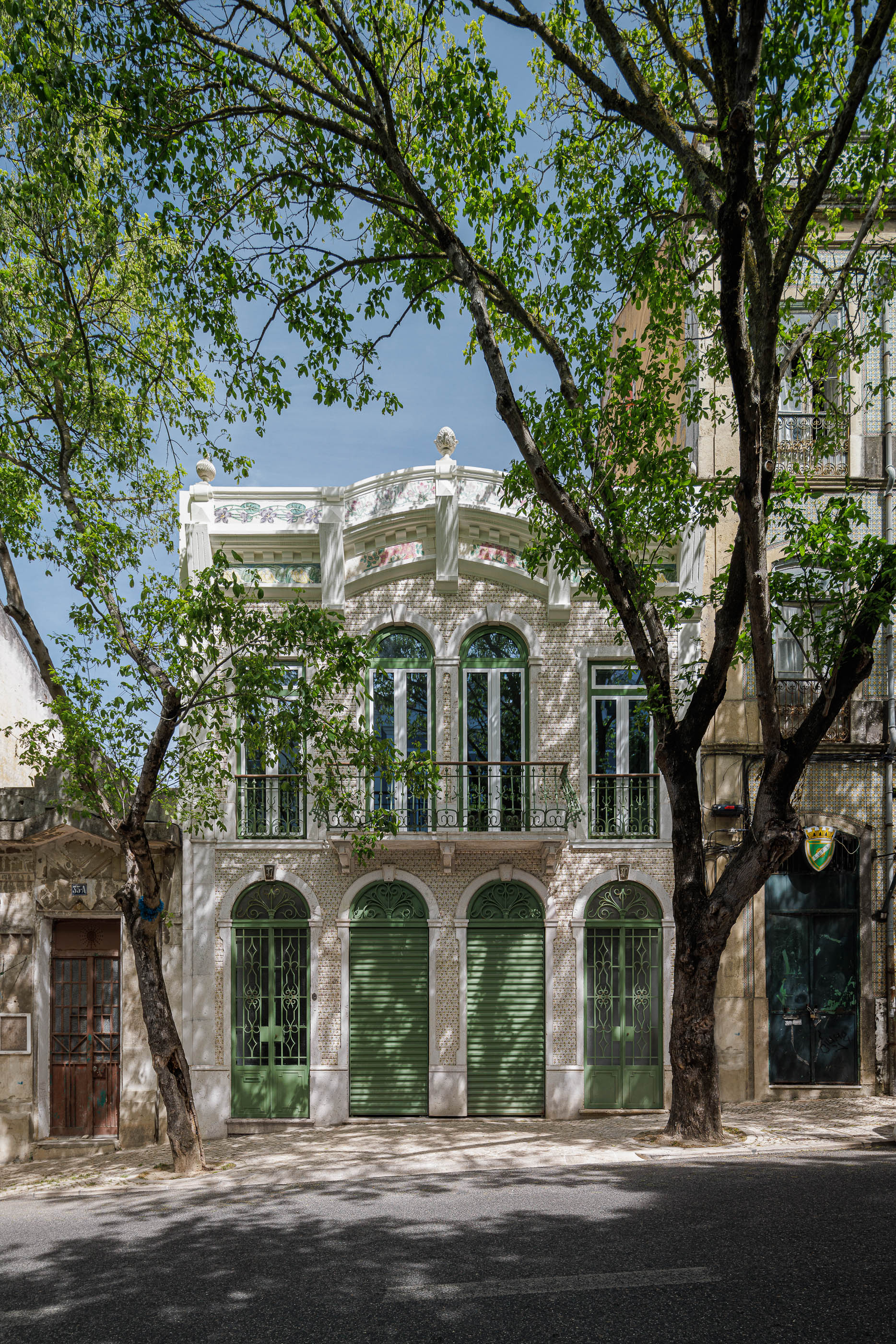Fachada: Edifício Art Nouveau com azulejos florais, varanda em ferro forjado e portões verdes. — Possidónio da Silva 37 arquitetura Fragmentos em Lisboa