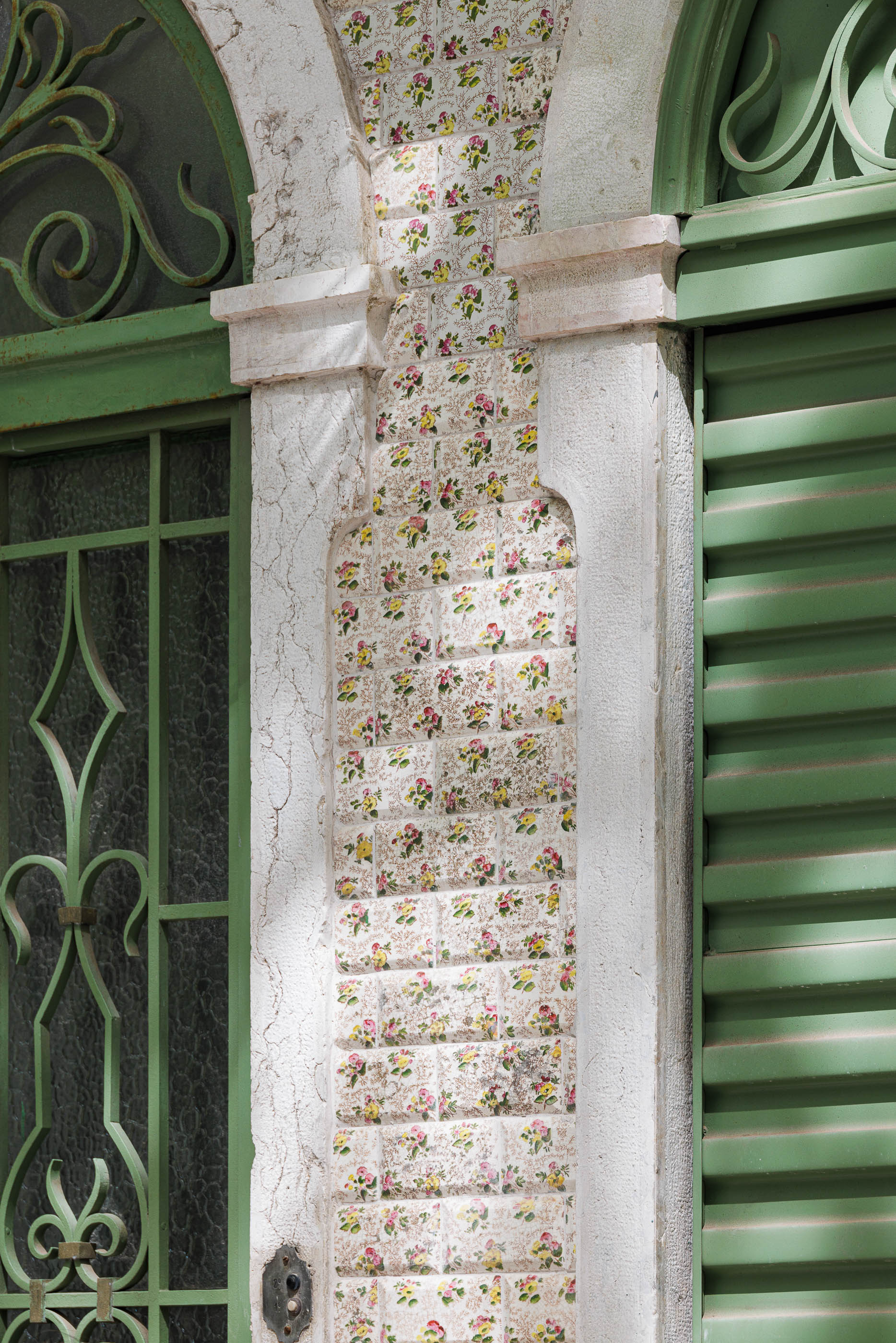 Fachada: Pormenor de azulejos florais emoldurando porta e portão, com detalhes em ferro forjado verde. — Possidónio da Silva 37 arquitetura Fragmentos em Lisboa