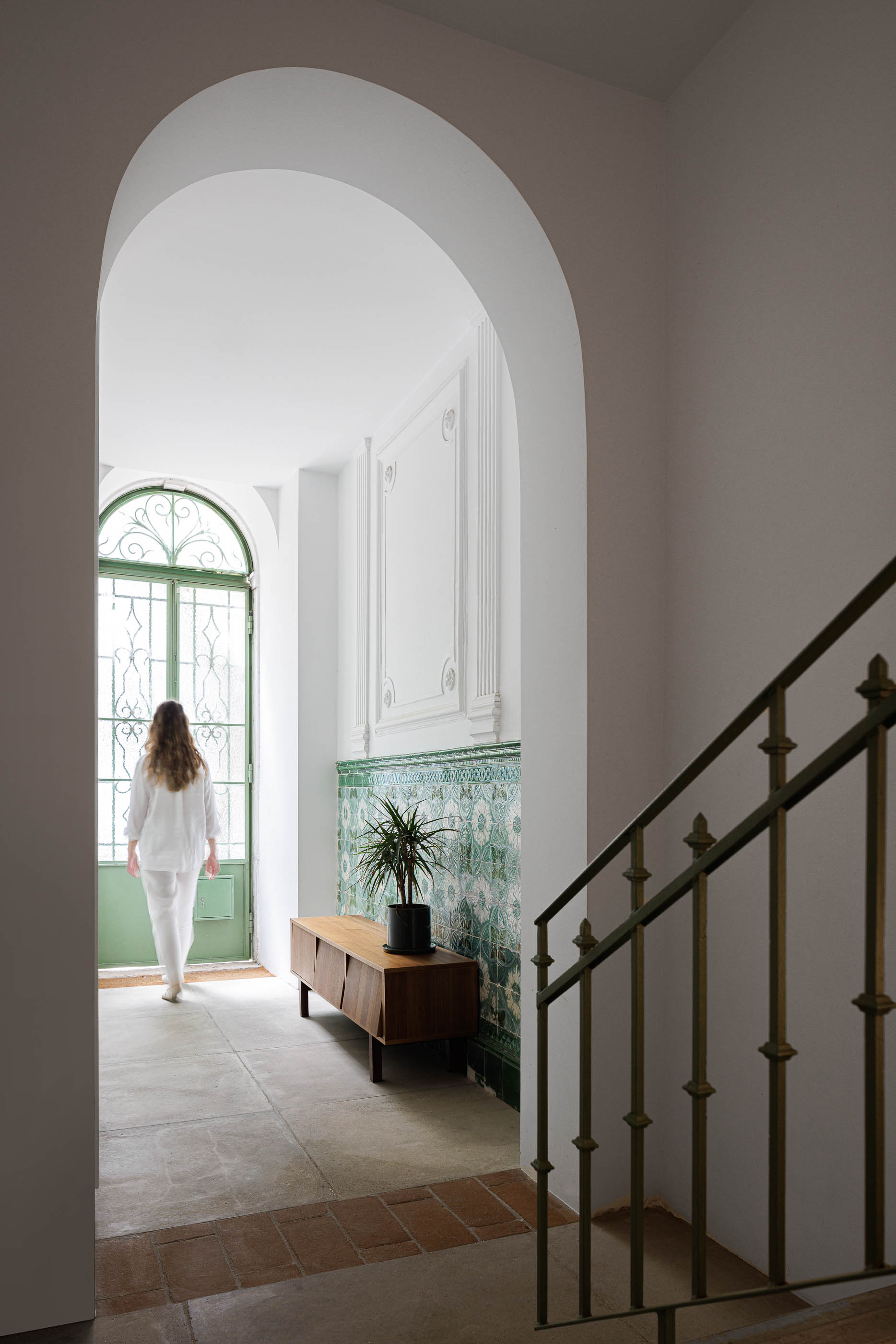 Hall de entrada: Arco branco conduzindo a porta verde, com painel de azulejos e consola de madeira. — Possidónio da Silva 37 arquitetura Fragmentos em Lisboa
