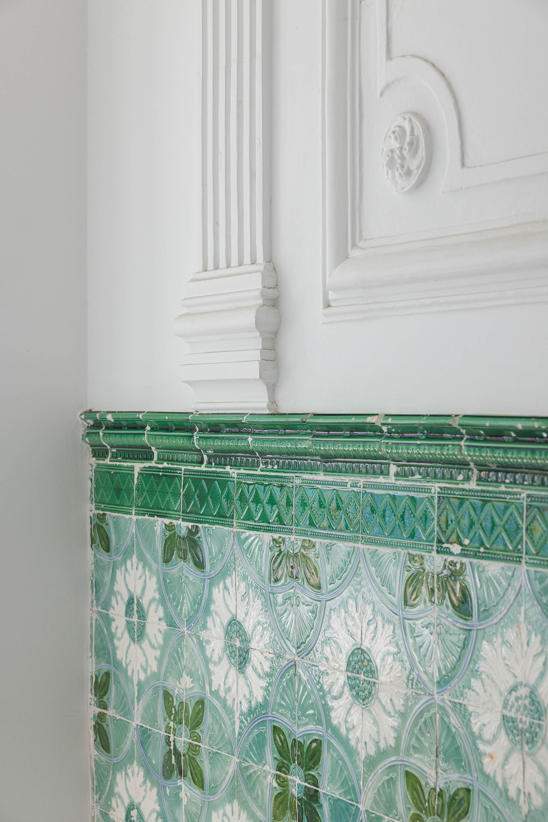 Hall de entrada: Detalhe de painel de azulejos verdes e brancos com motivos florais, junto a parede branca. — Possidónio da Silva 37 arquitetura Fragmentos em Lisboa