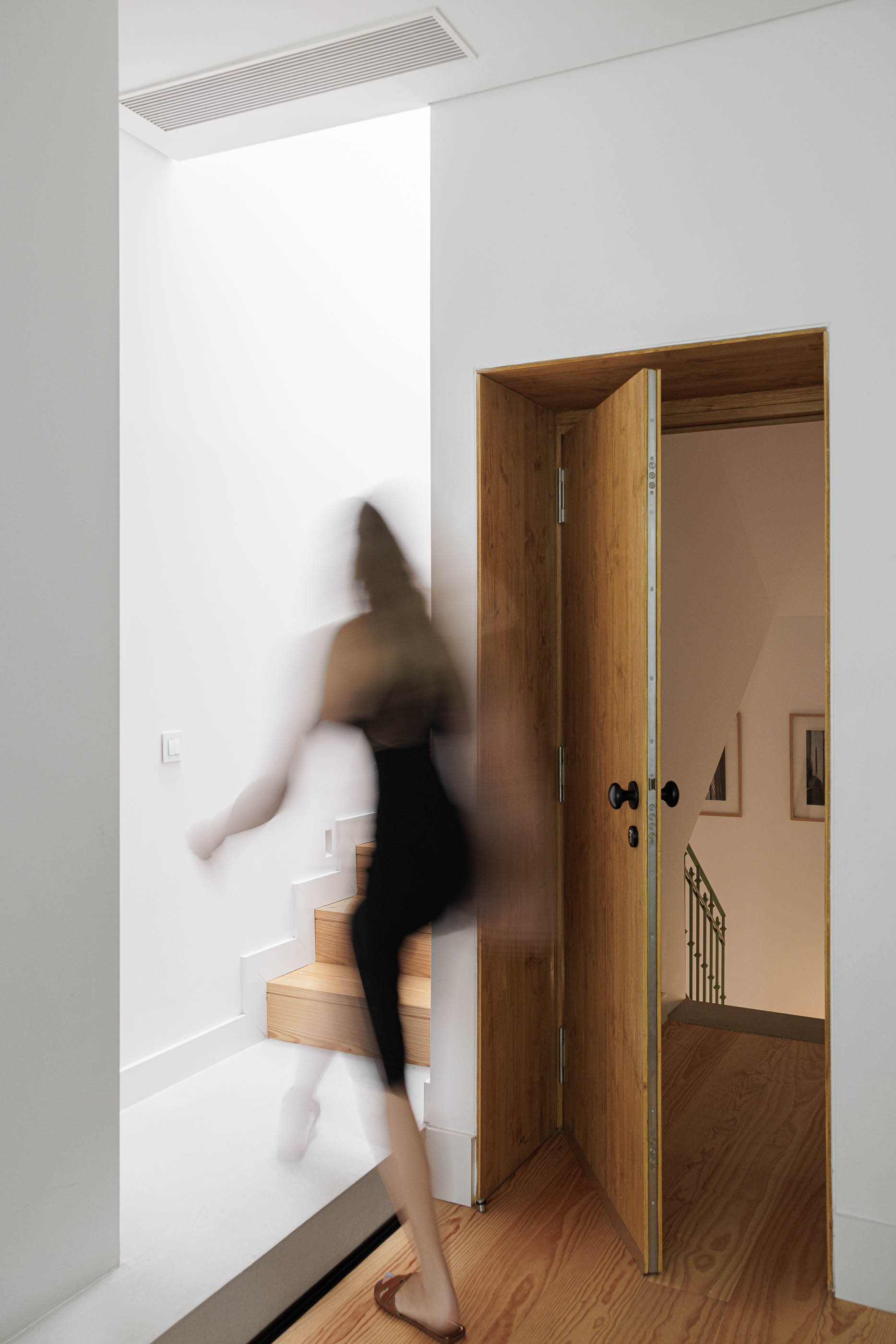 Escadas: Escadas de madeira com luz zenital, porta de madeira clara e pessoa a subir. — Possidónio da Silva 37 arquitetura Fragmentos em Lisboa