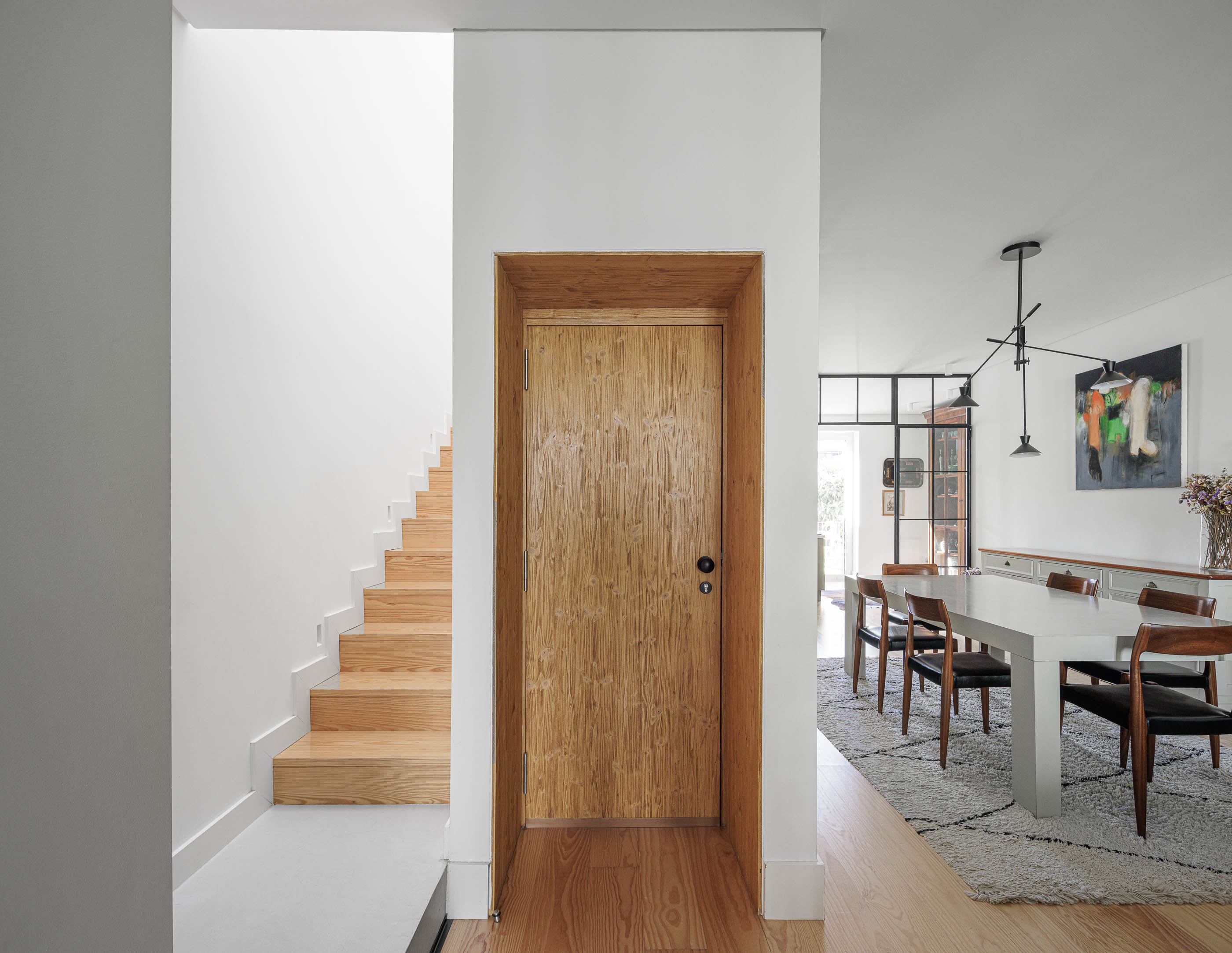 Escadas: Escadas de madeira clara, porta de madeira e vista para sala de jantar com alcatifa. — Possidónio da Silva 37 arquitetura Fragmentos em Lisboa