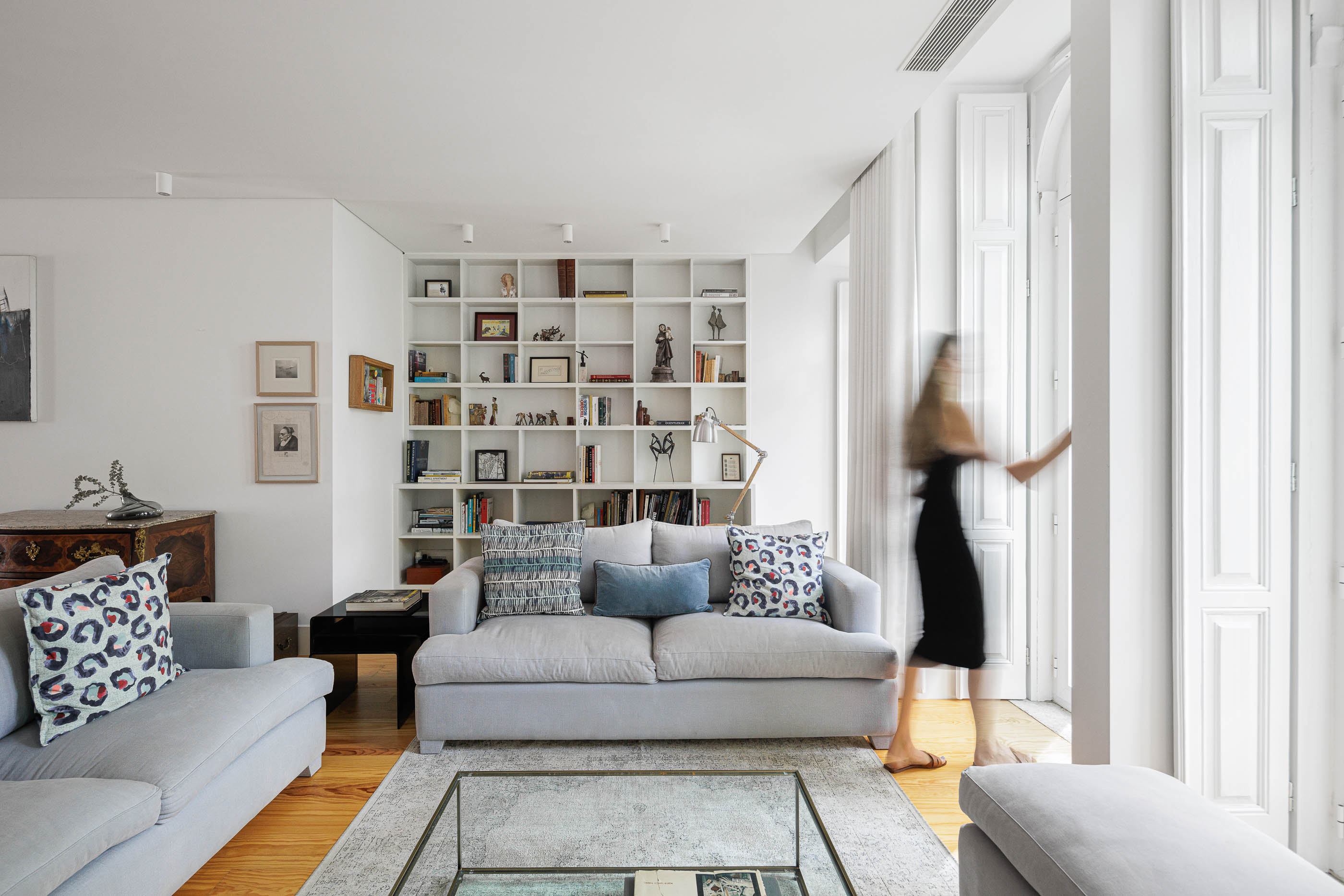 Sala de estar: Sofás cinzentos, estante branca com objetos decorativos e pavimento de madeira. — Possidónio da Silva 37 arquitetura Fragmentos em Lisboa
