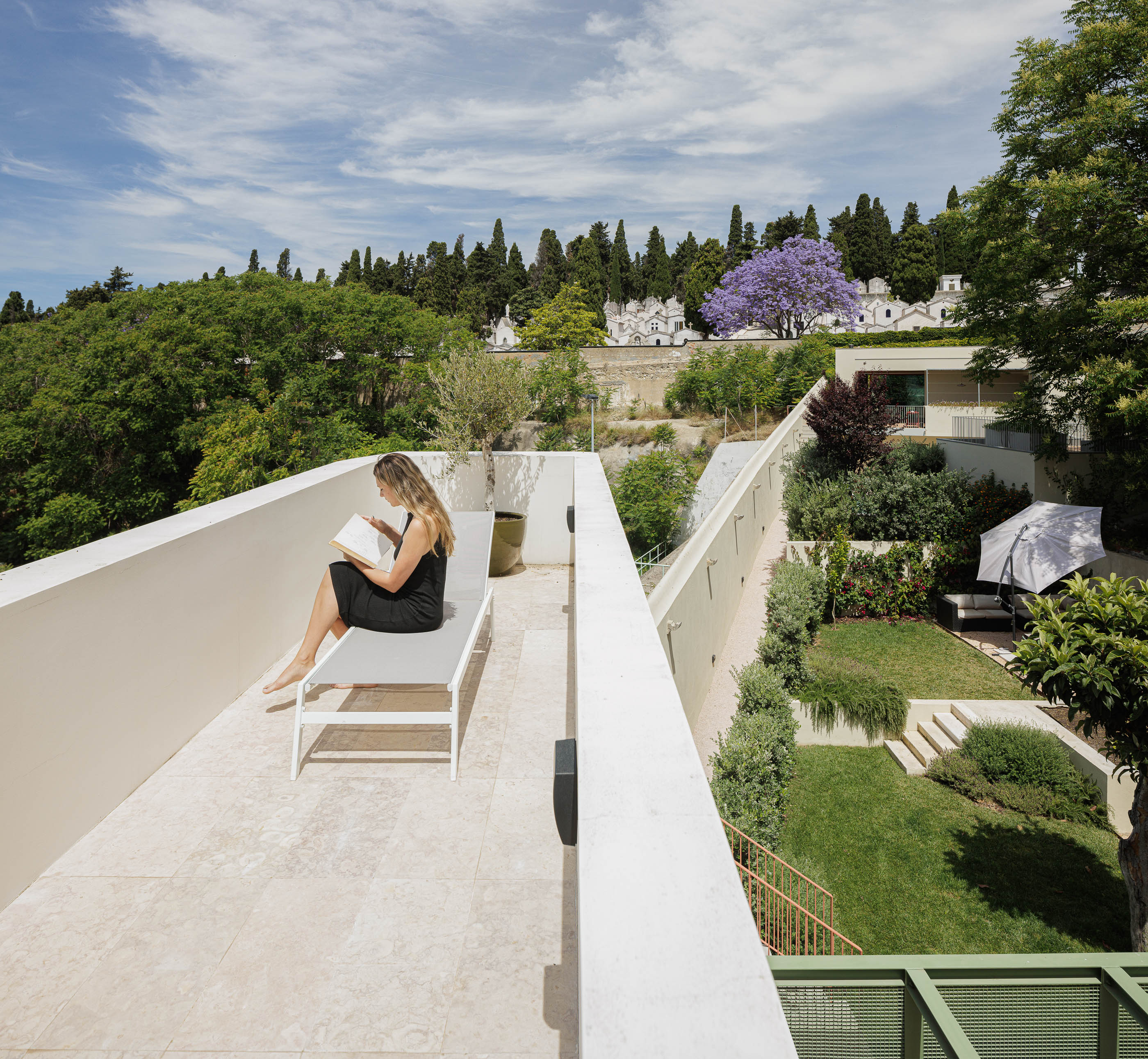 Terraço: Espreguiçadeira branca, jardim relvado e vista para o cemitério e vegetação densa. — Possidónio da Silva 37 arquitetura Fragmentos em Lisboa