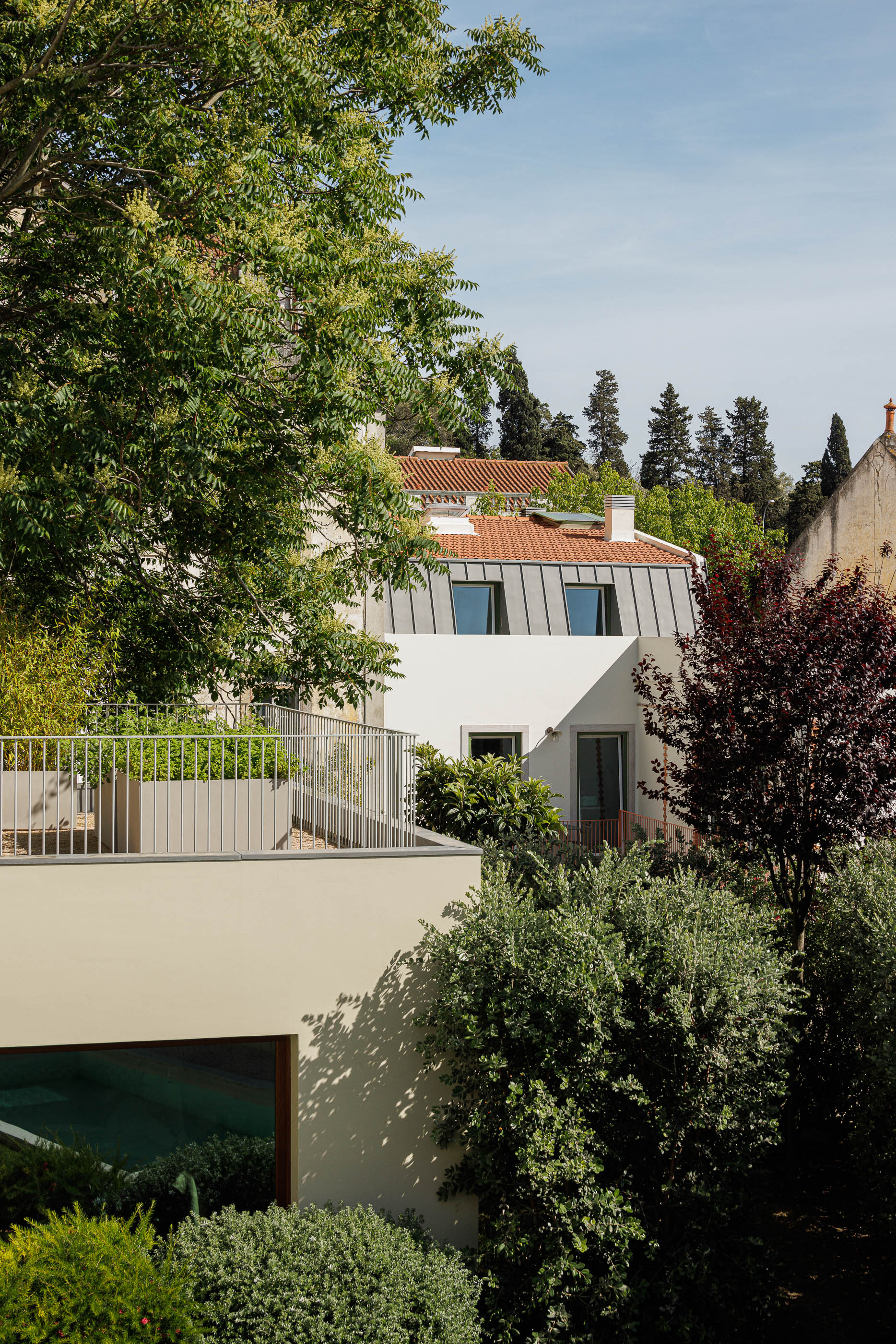 Exterior: Vista da casa com telhado cinzento, terraço e vegetação densa. — Possidónio da Silva 37 arquitetura Fragmentos em Lisboa