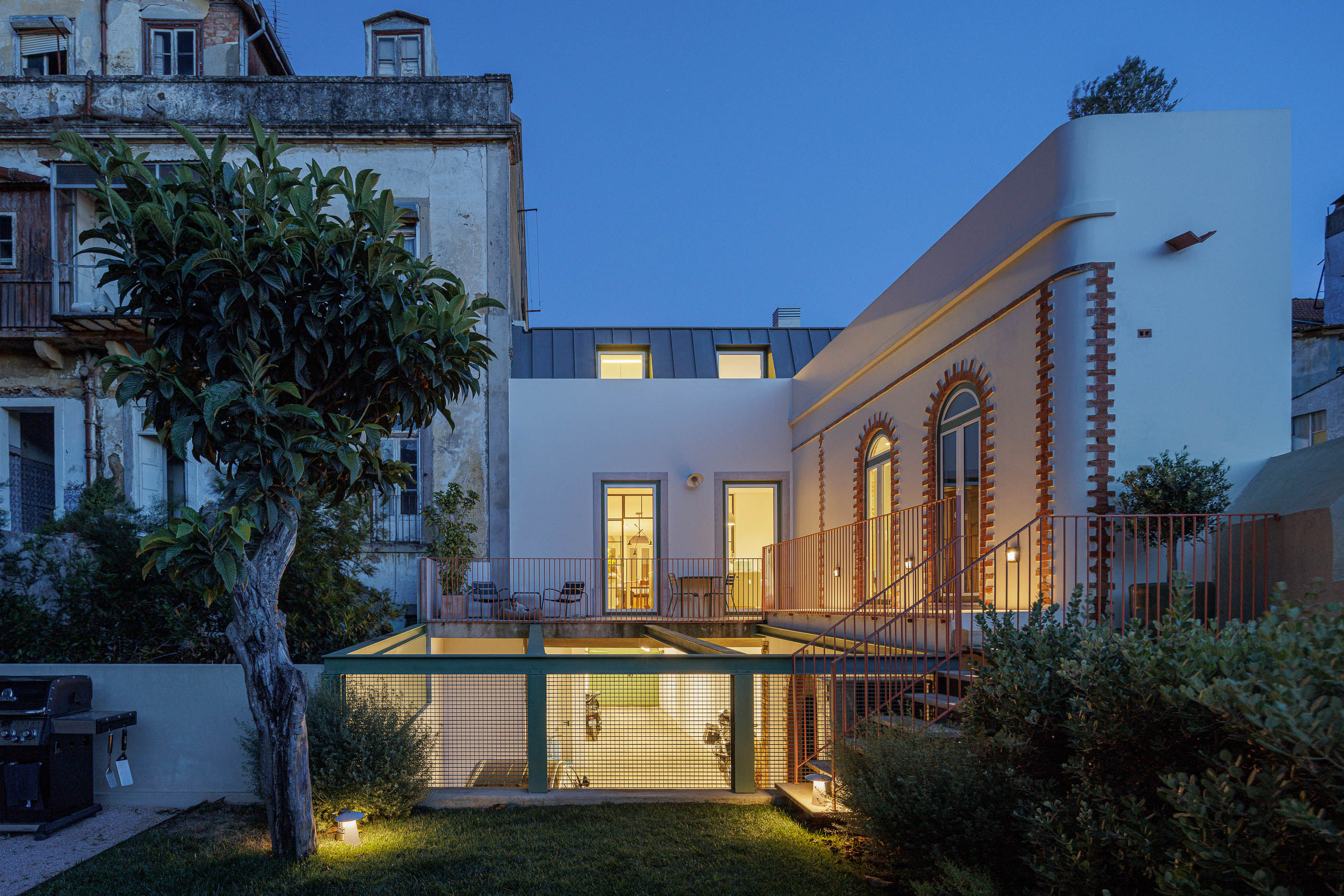 Exterior: Vista noturna da casa com terraço, jardim relvado e estrutura metálica verde. — Possidónio da Silva 37 arquitetura Fragmentos em Lisboa