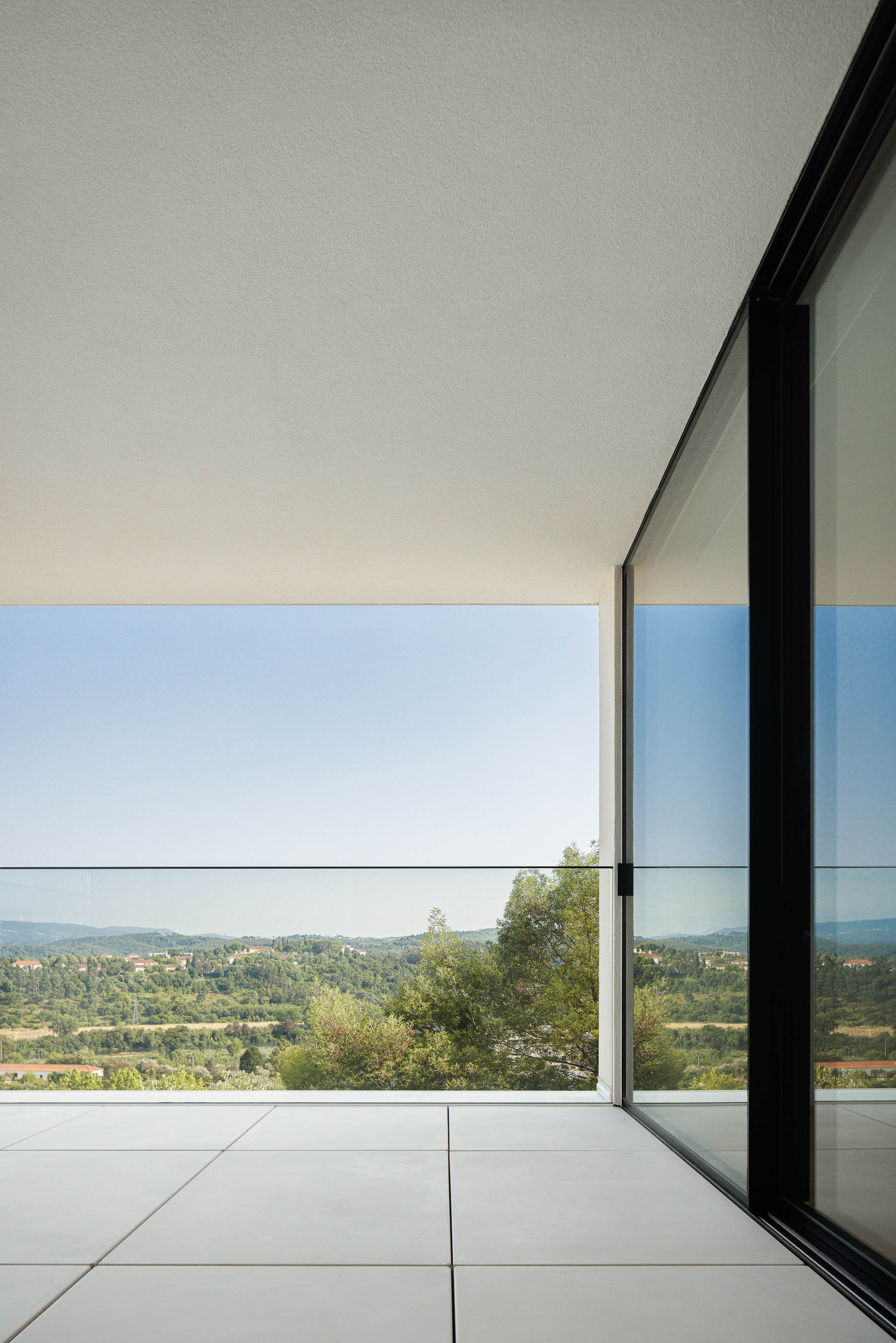 Varanda com pavimento cerâmico branco e guarda em vidro. Vista panorâmica sobre a paisagem. — Casa JC arquitetura Mário Alves Arquitecto em Coimbra