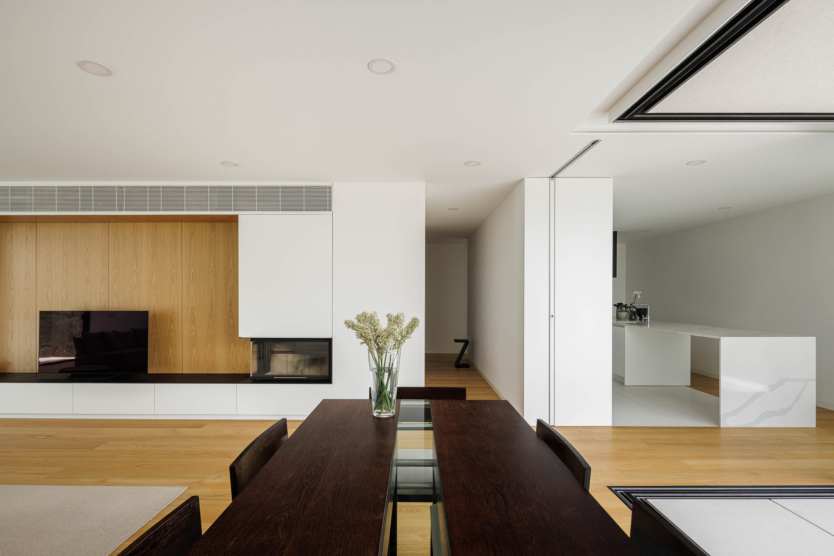 Sala de jantar com mesa de madeira escura e cadeiras. Vista para a sala de estar e cozinha. — Casa JC arquitetura Mário Alves Arquitecto em Coimbra