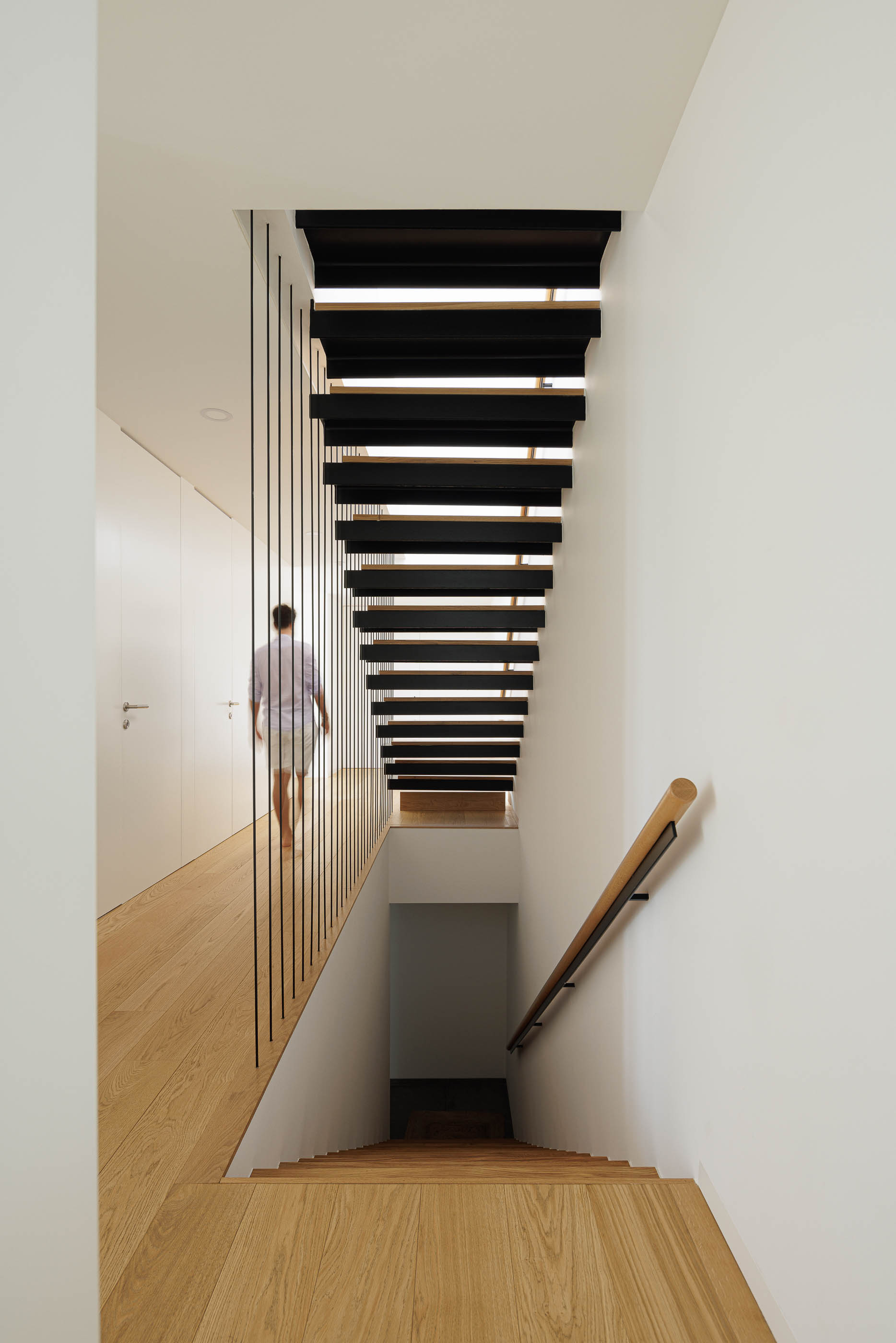Escadas com degraus em madeira e estrutura metálica preta. Corrimão em madeira clara e pavimento em madeira. — Casa JC arquitetura Mário Alves Arquitecto em Coimbra