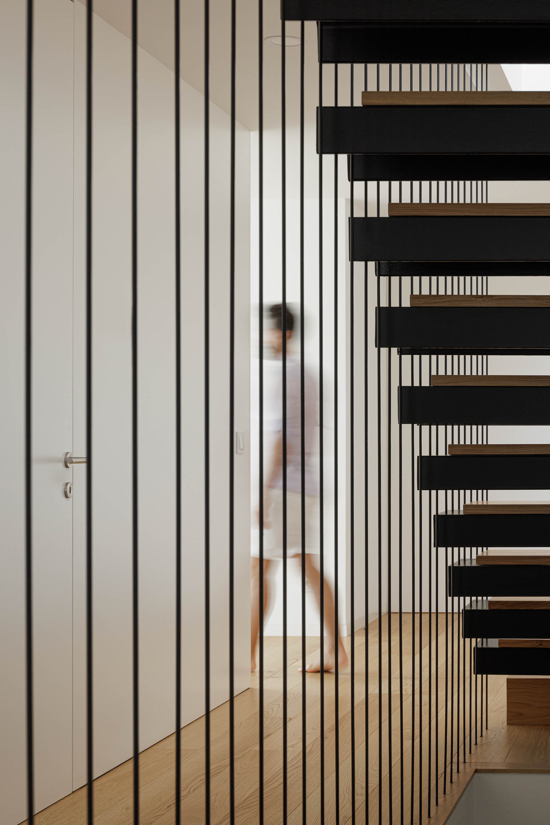 Escadas com guarda em varões metálicos pretos. Pavimento em madeira clara e portas brancas. — Casa JC arquitetura Mário Alves Arquitecto em Coimbra