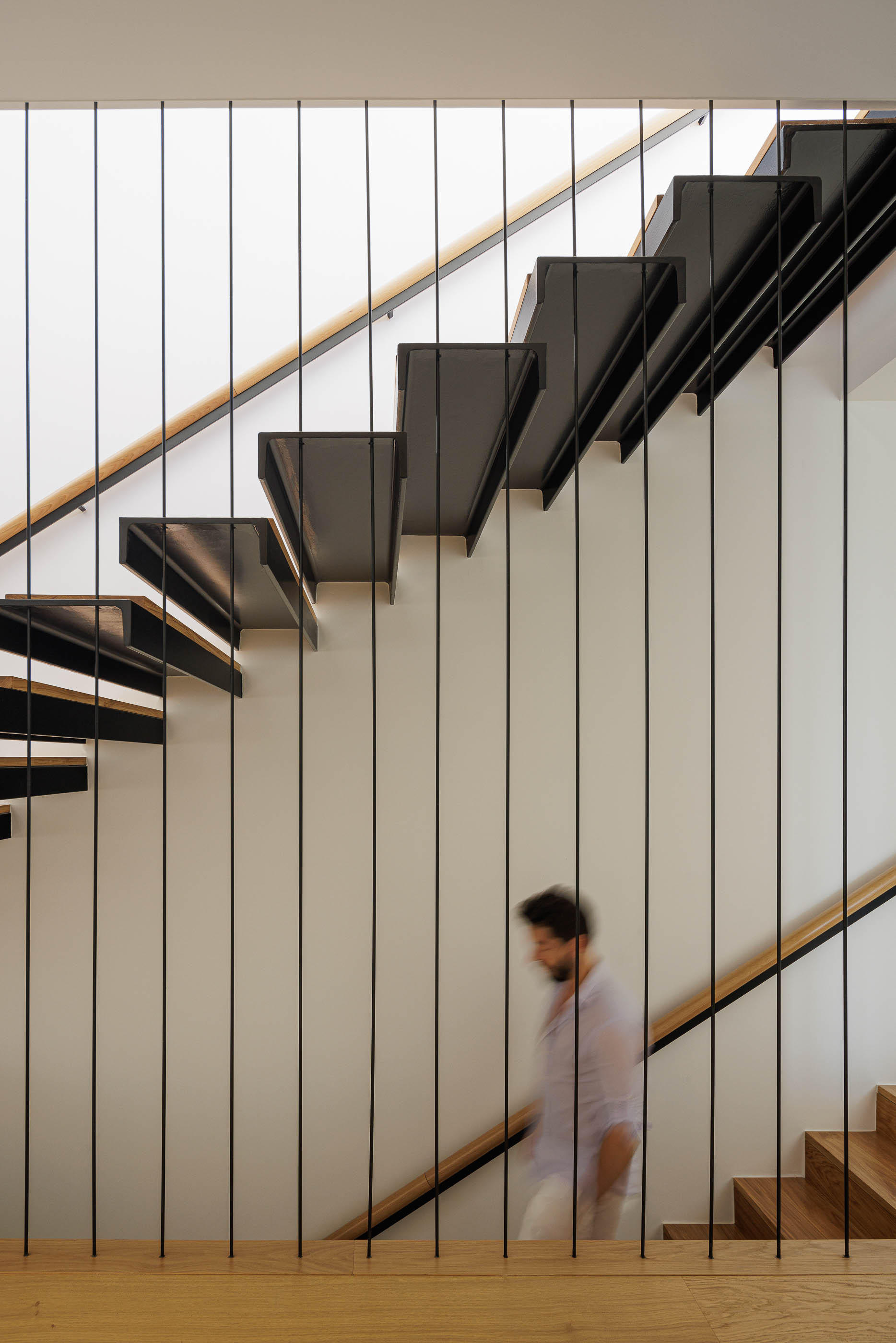 Escadas com degraus em madeira e estrutura metálica preta. Corrimão em madeira clara. — Casa JC arquitetura Mário Alves Arquitecto em Coimbra