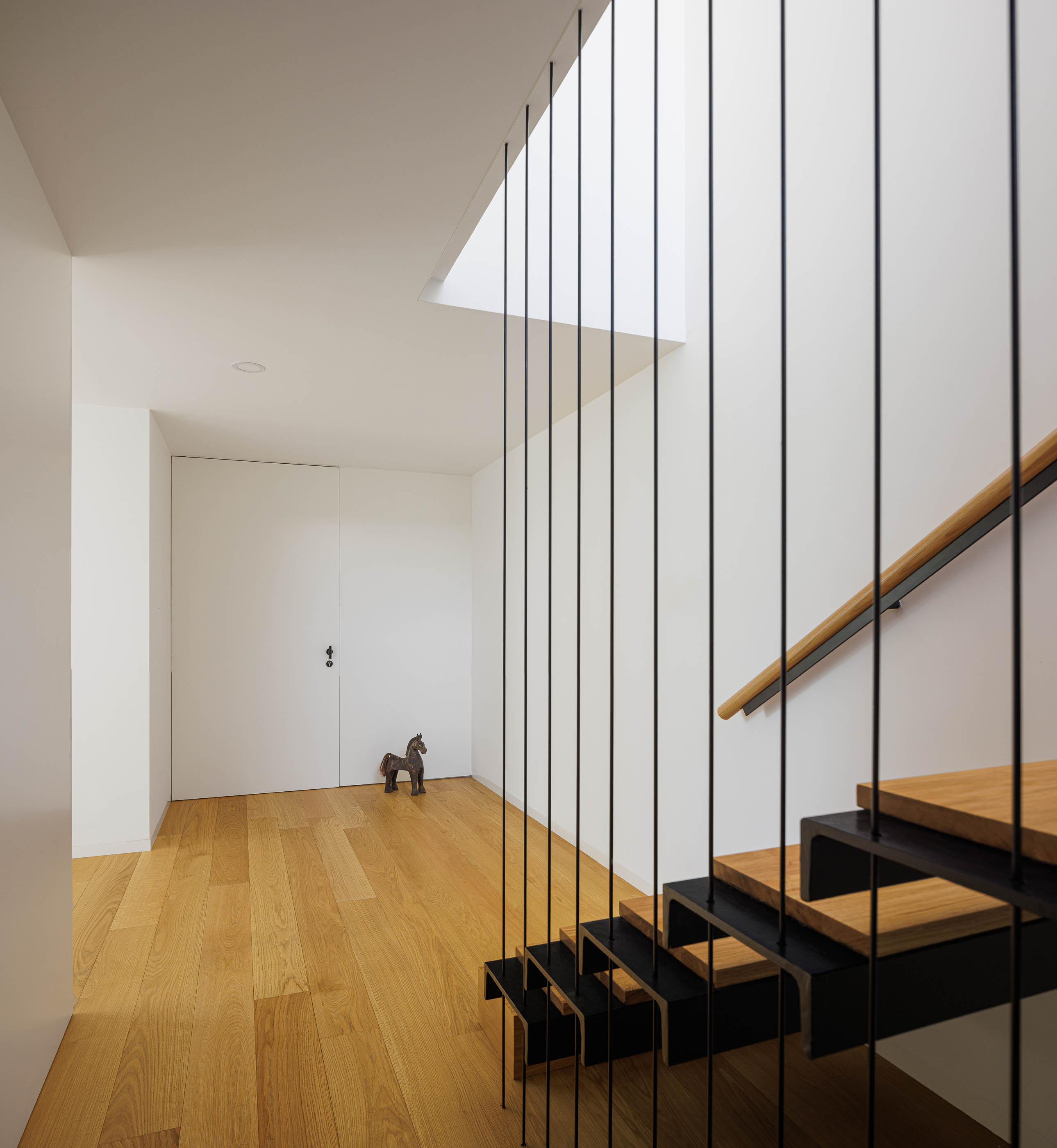 Escadas com degraus em madeira e estrutura metálica preta. Claraboia no teto e pavimento em madeira. — Casa JC arquitetura Mário Alves Arquitecto em Coimbra