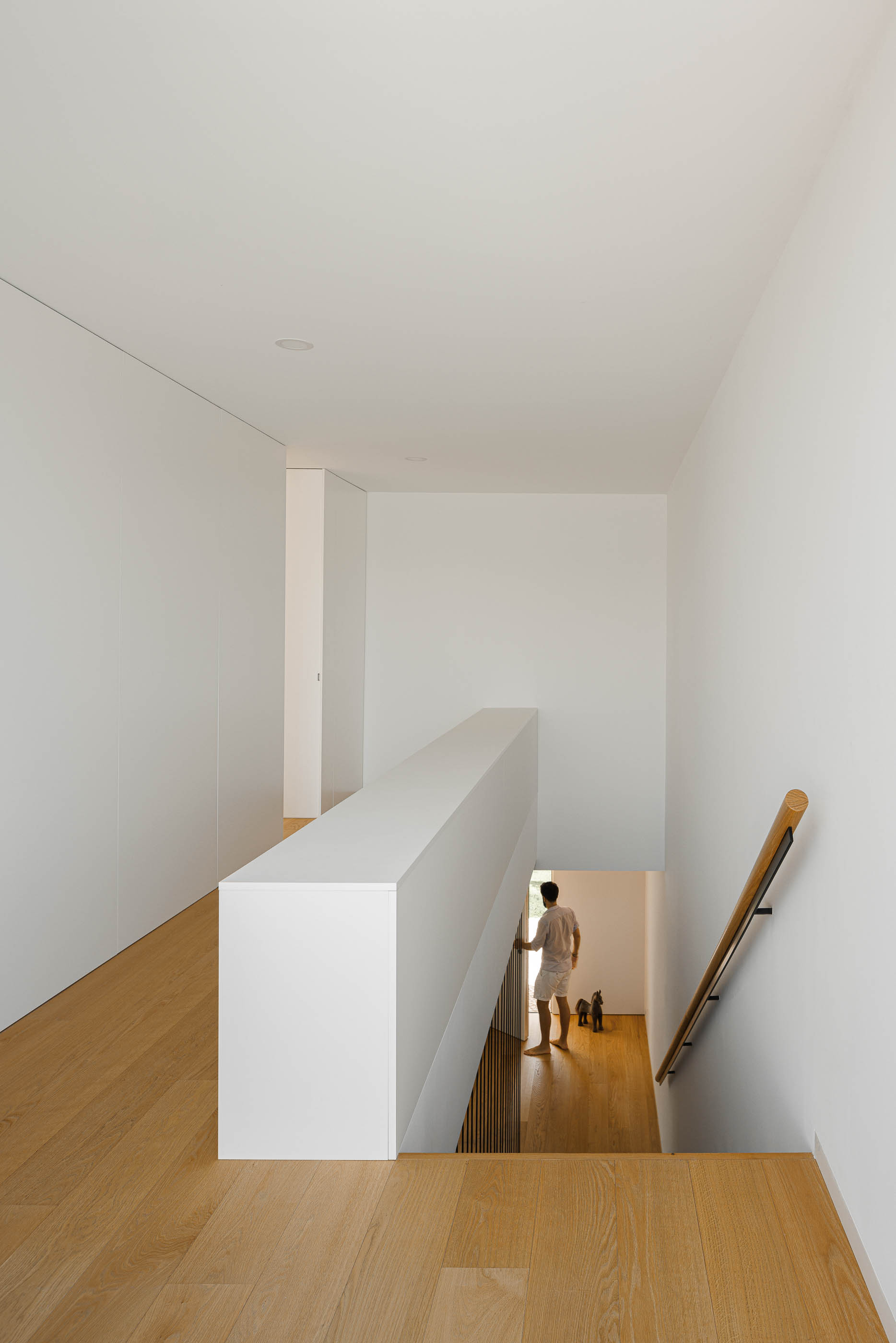 Hall com escadas e pavimento em madeira clara. Guarda em branco e portas brancas. — Casa JC arquitetura Mário Alves Arquitecto em Coimbra