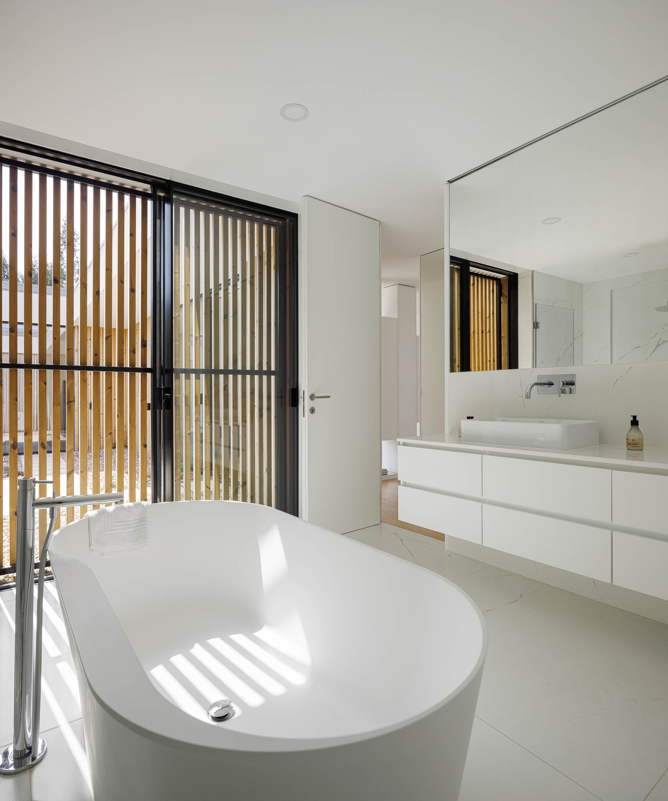 Casa de banho com banheira branca e lavatório suspenso. Revestimento em mármore branco e pavimento cerâmico. — Casa JC arquitetura Mário Alves Arquitecto em Coimbra