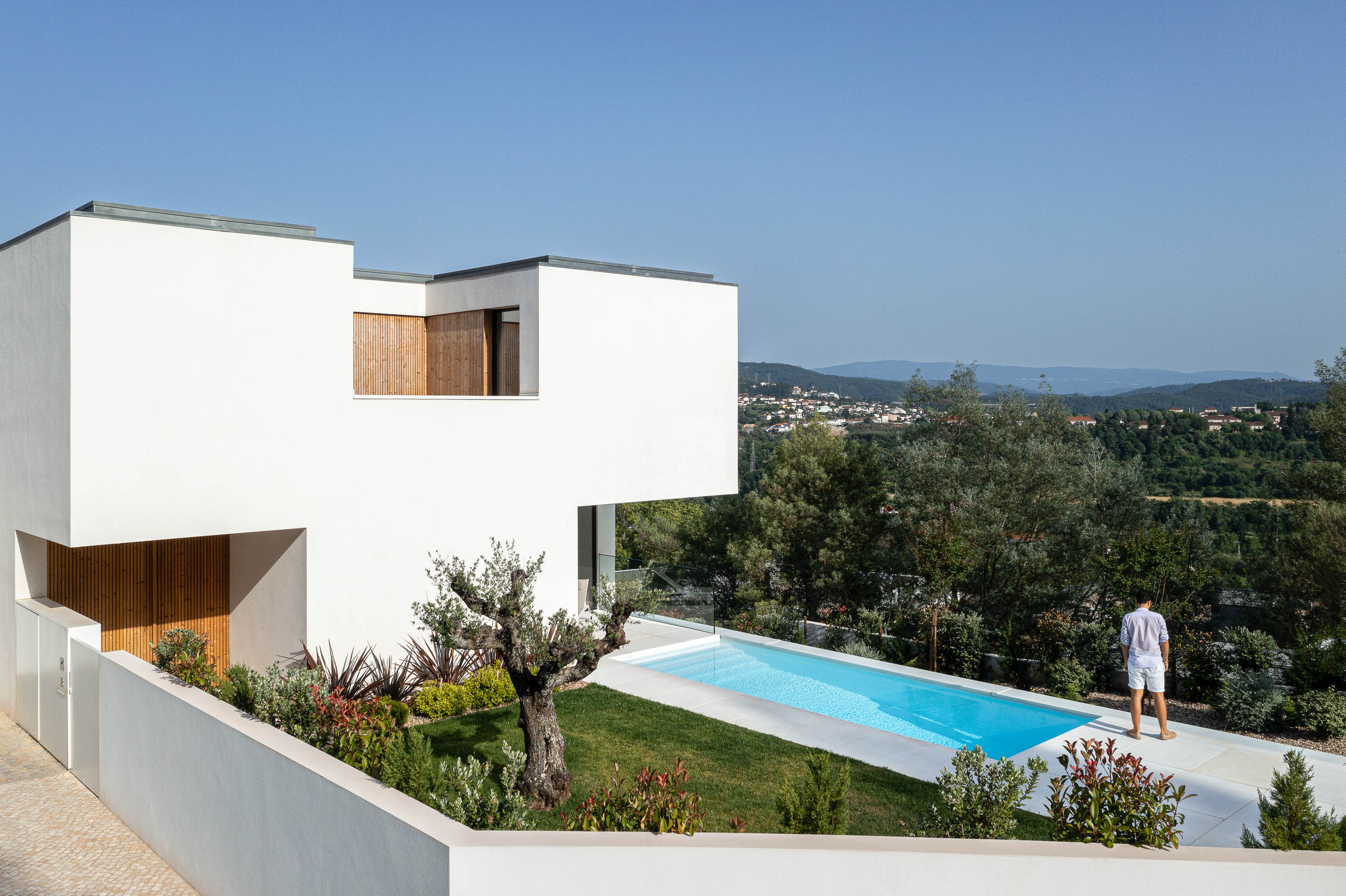 Exterior da casa com piscina e jardim. Arquitetura moderna com volumes brancos e detalhes em madeira. — Casa JC arquitetura Mário Alves Arquitecto em Coimbra