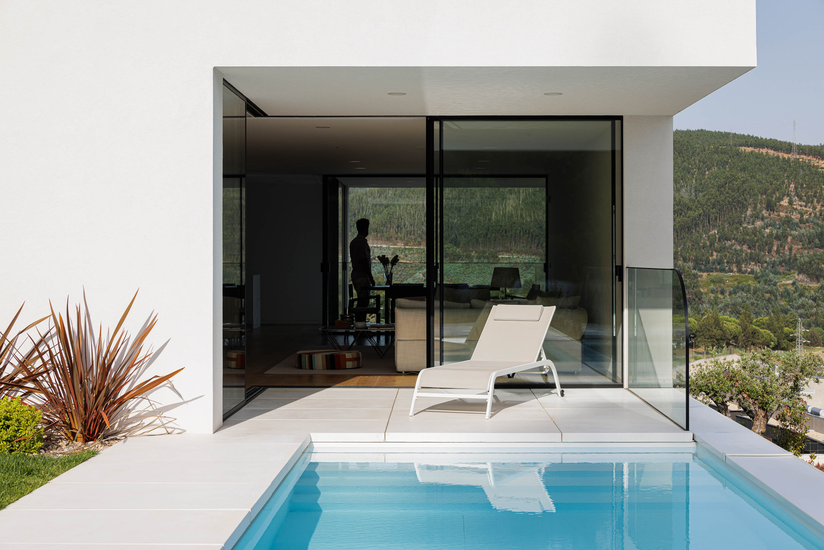 Exterior da casa com piscina e espreguiçadeira. Acesso direto à sala de estar através de grandes janelas. — Casa JC arquitetura Mário Alves Arquitecto em Coimbra