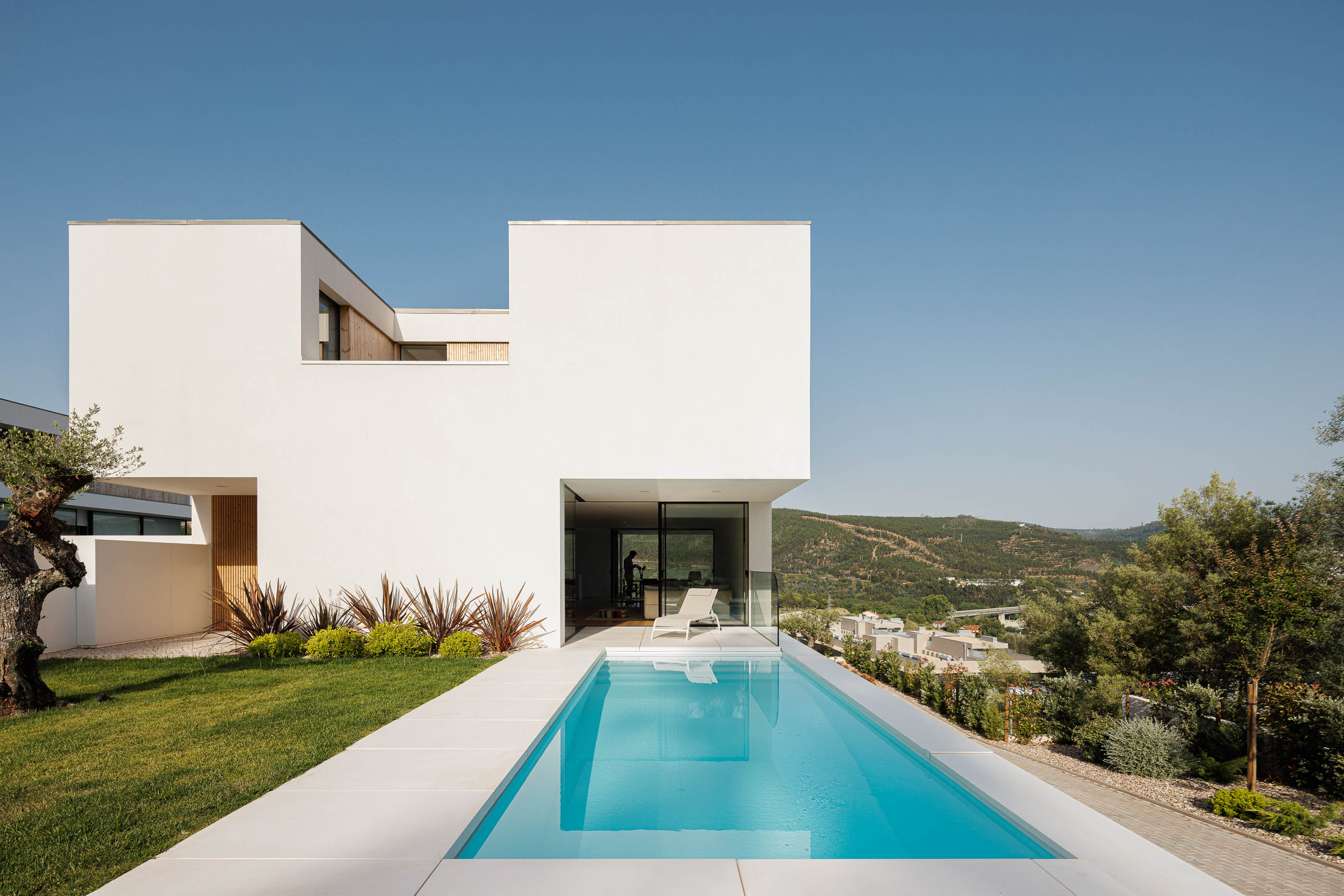 Exterior da casa com piscina e jardim. Arquitetura moderna com volumes brancos e detalhes em madeira. — Casa JC arquitetura Mário Alves Arquitecto em Coimbra